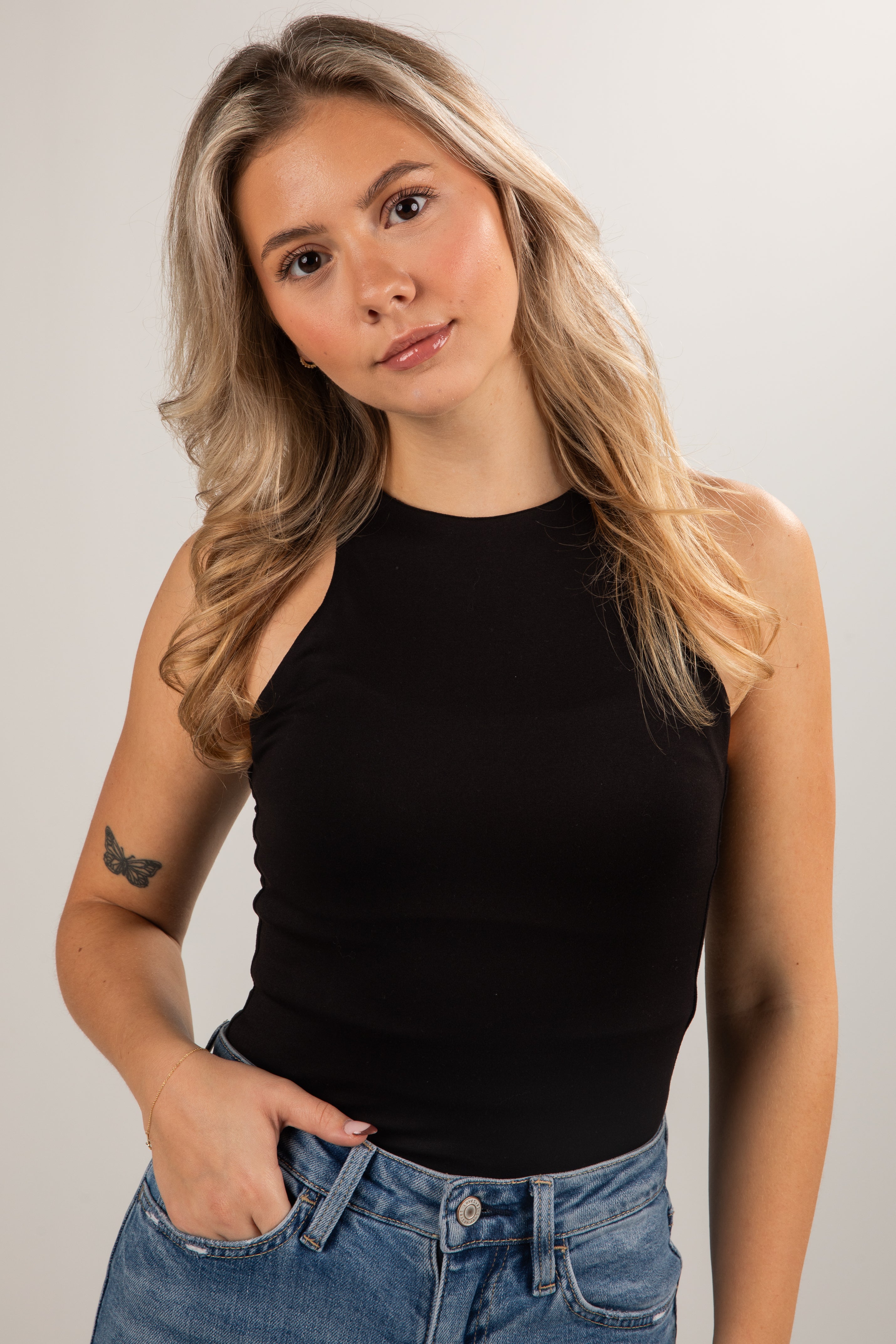 Woman wearing a black tank top and blue jeans against a plain background