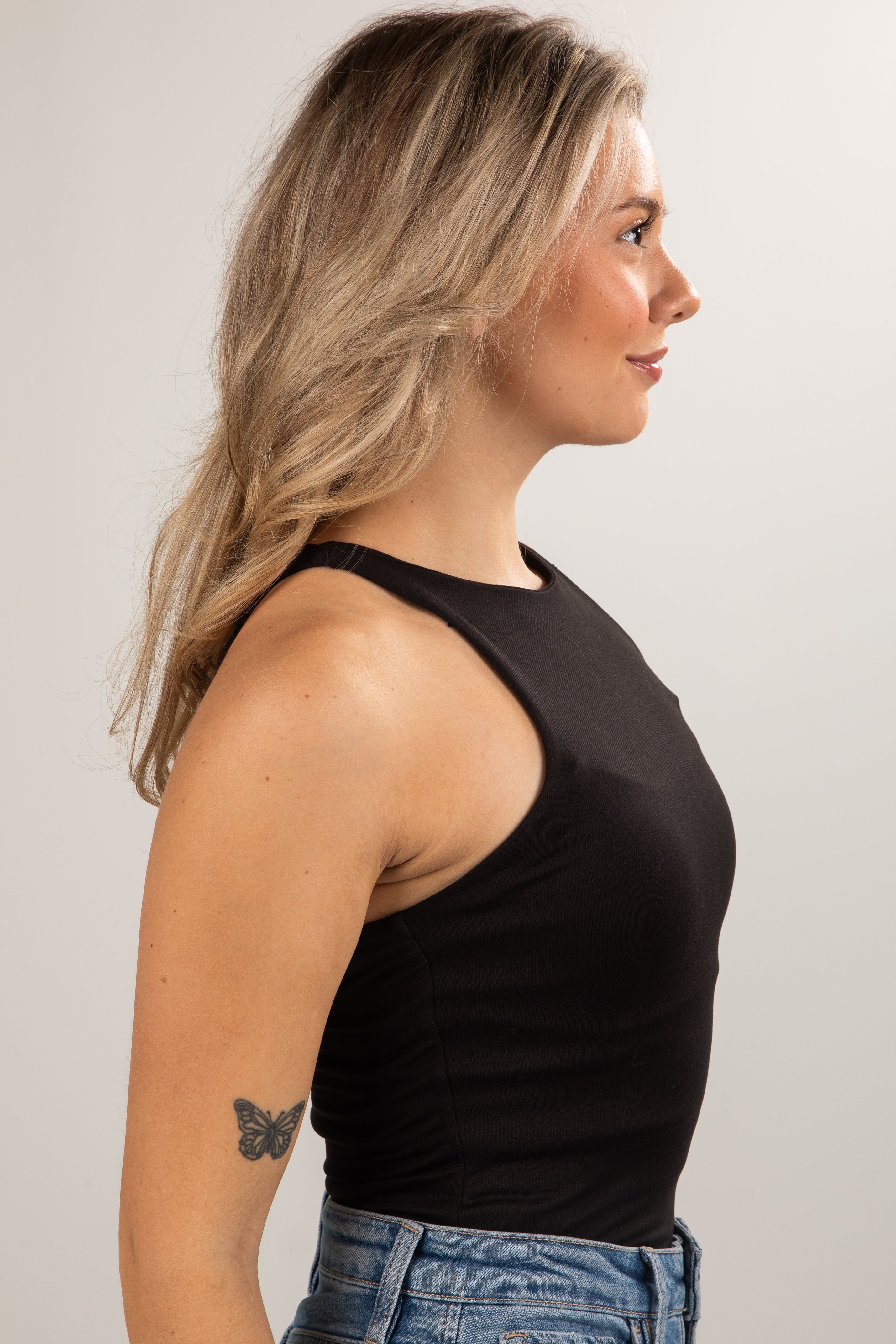 Woman wearing a black tank top and blue jeans against a plain background