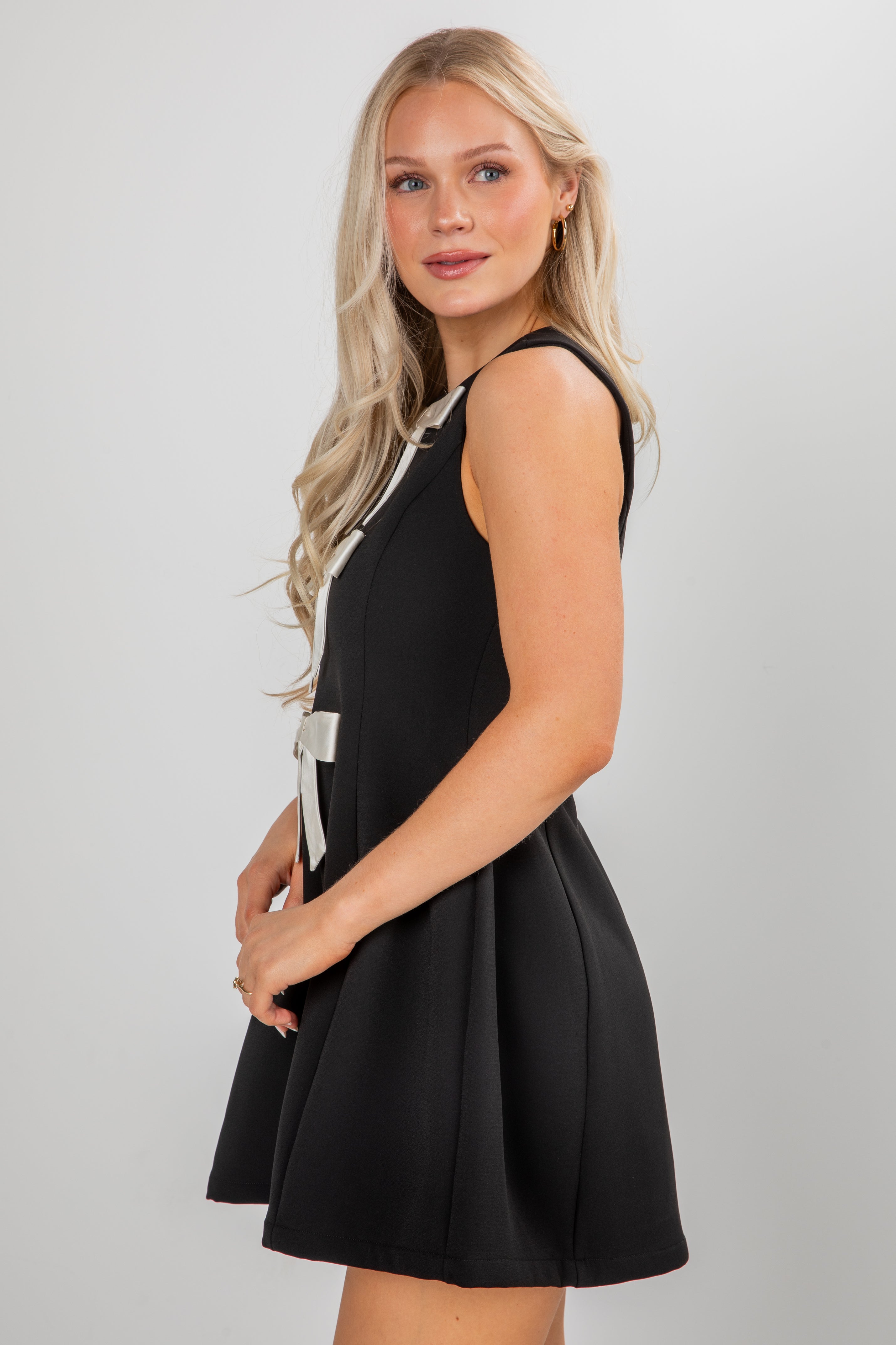 Woman wearing a black dress with a white bow on a plain background