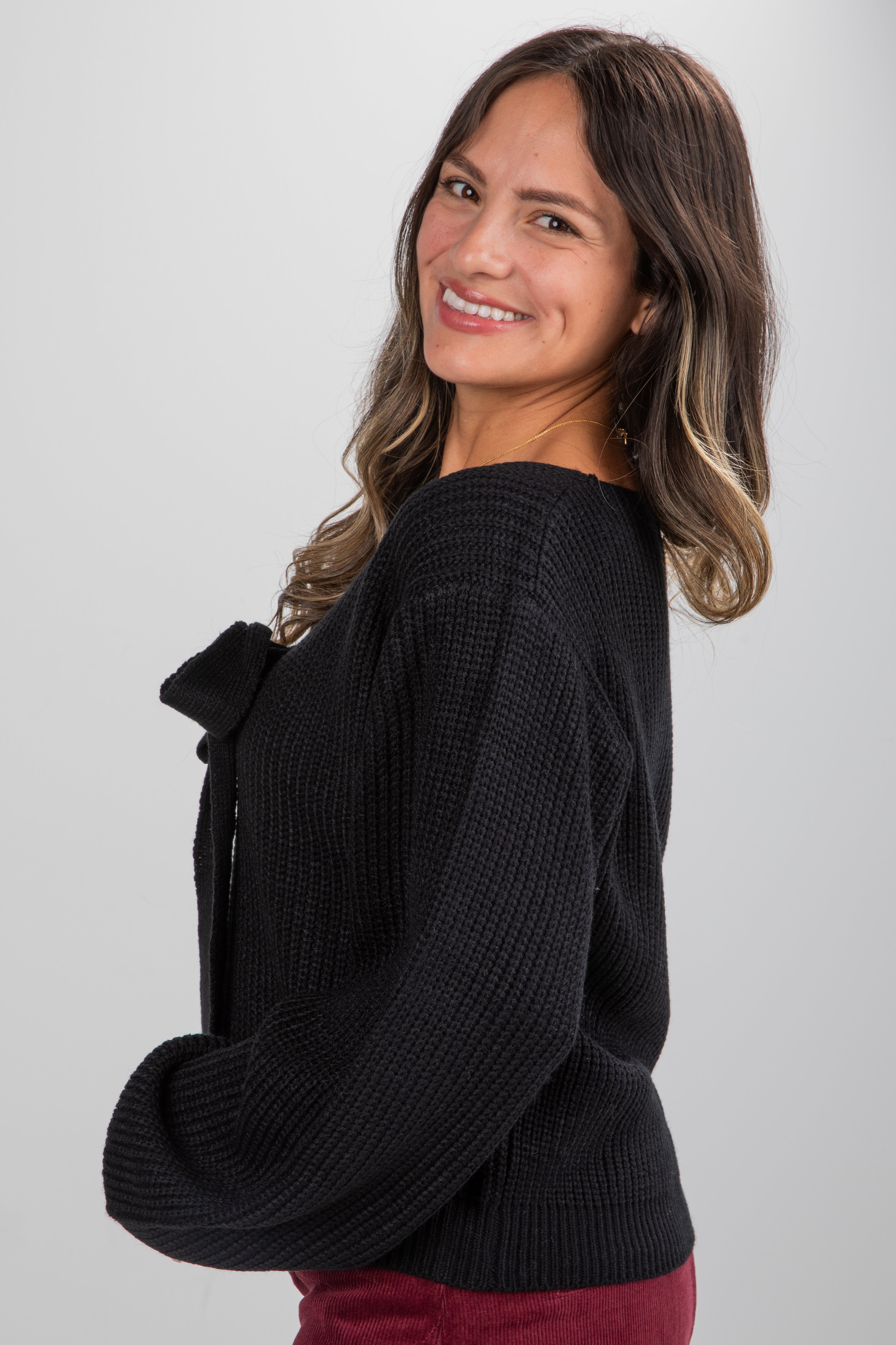 Woman wearing a black sweater with a bow detail on a plain background