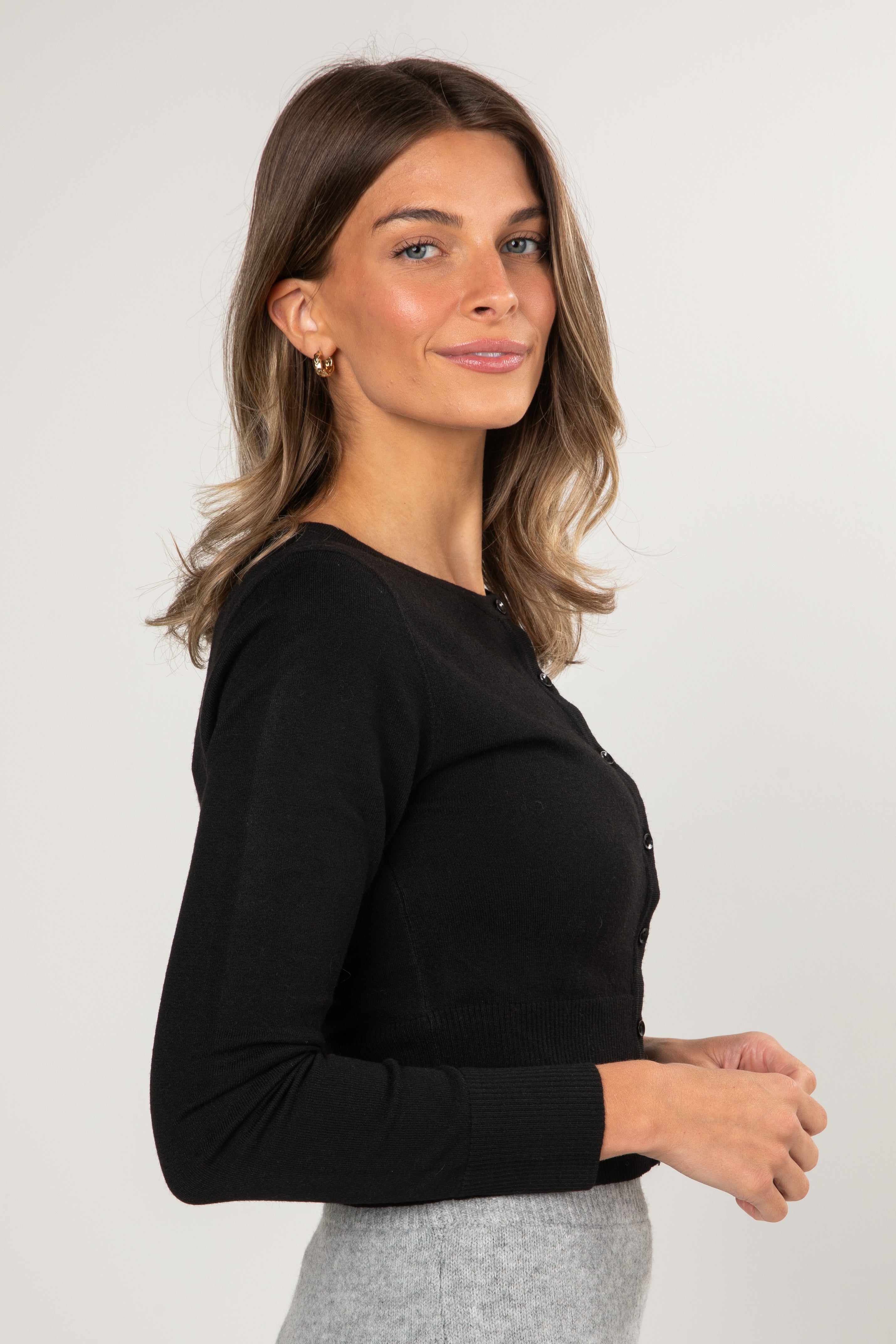 Woman wearing a black long-sleeve top and gray pants on a white background