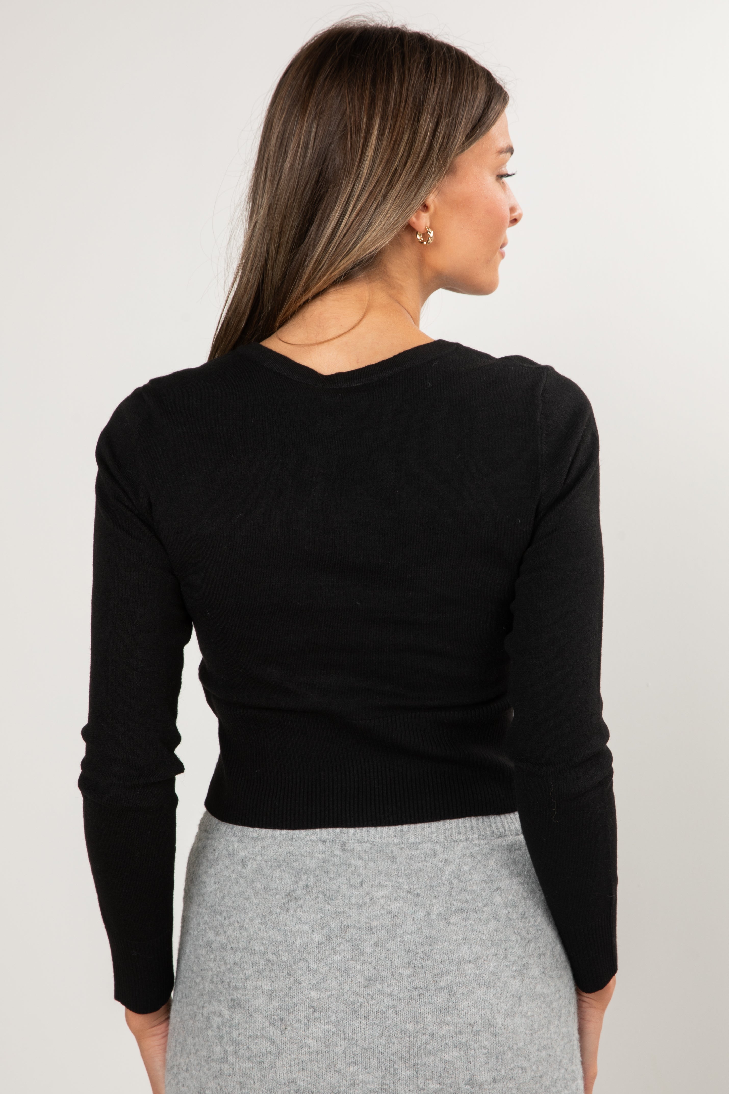 Woman wearing a black long-sleeve top and gray skirt on a white background
