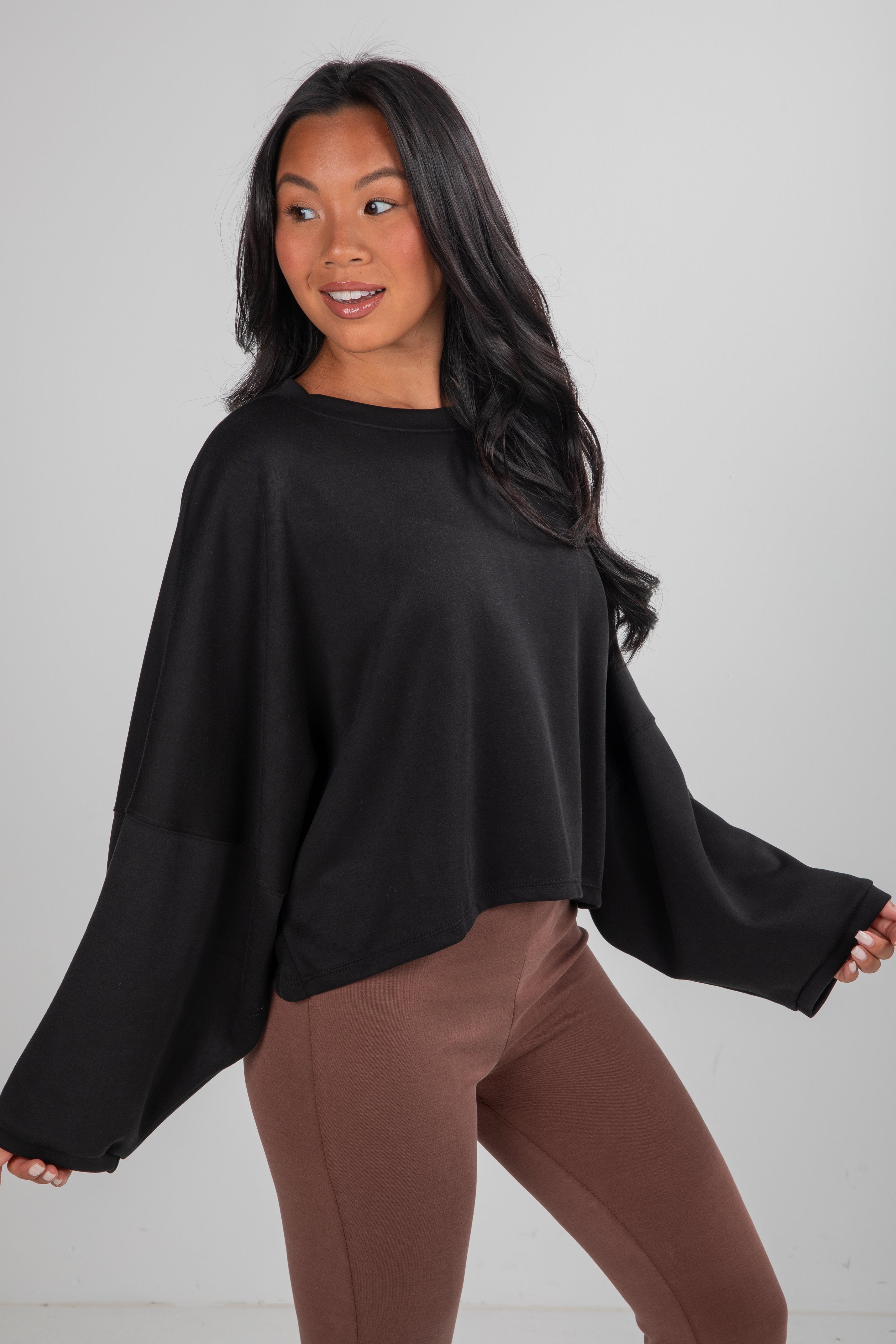 Woman wearing a black top and brown pants against a white background