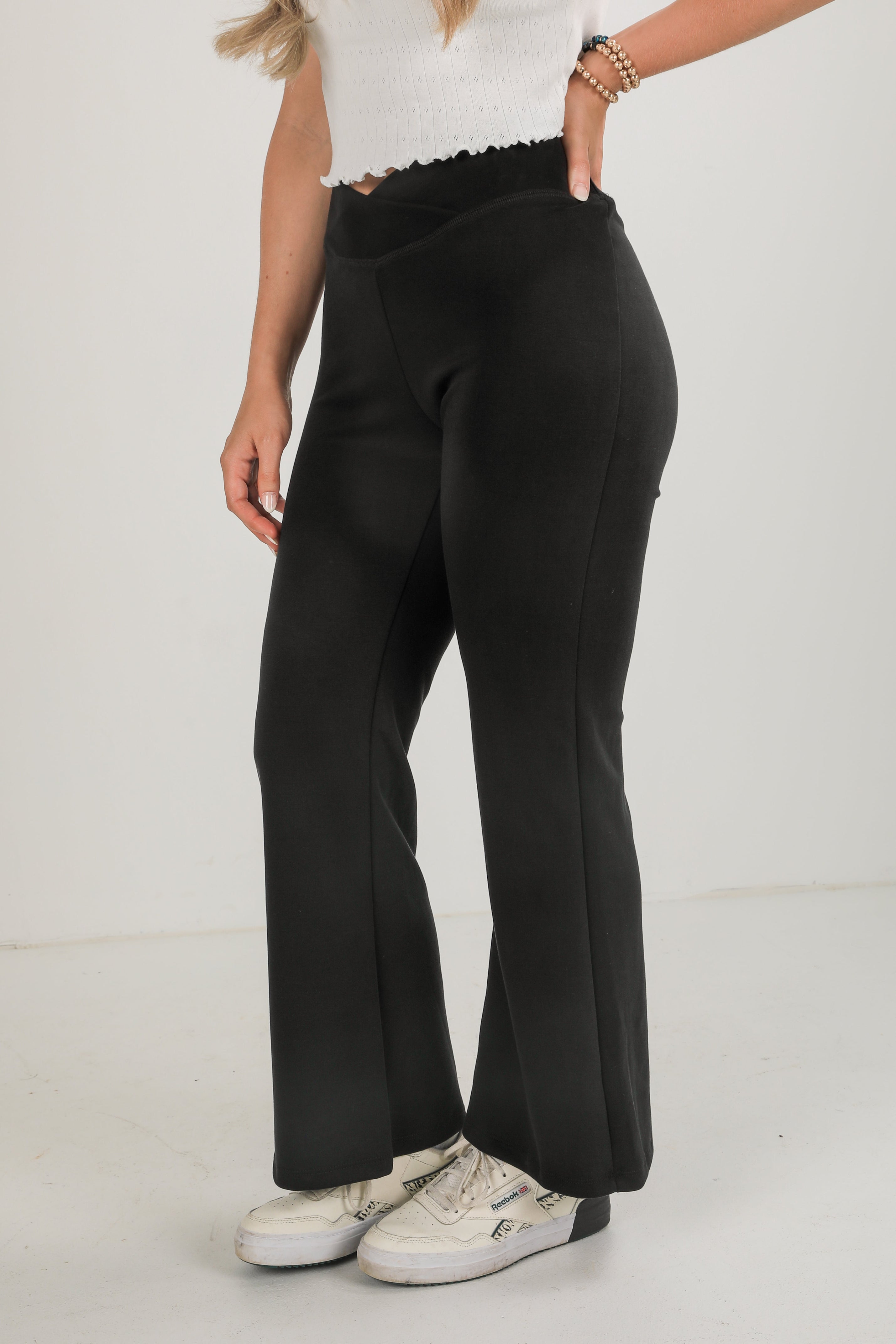 Person wearing black wide-leg pants and white sneakers on a light background