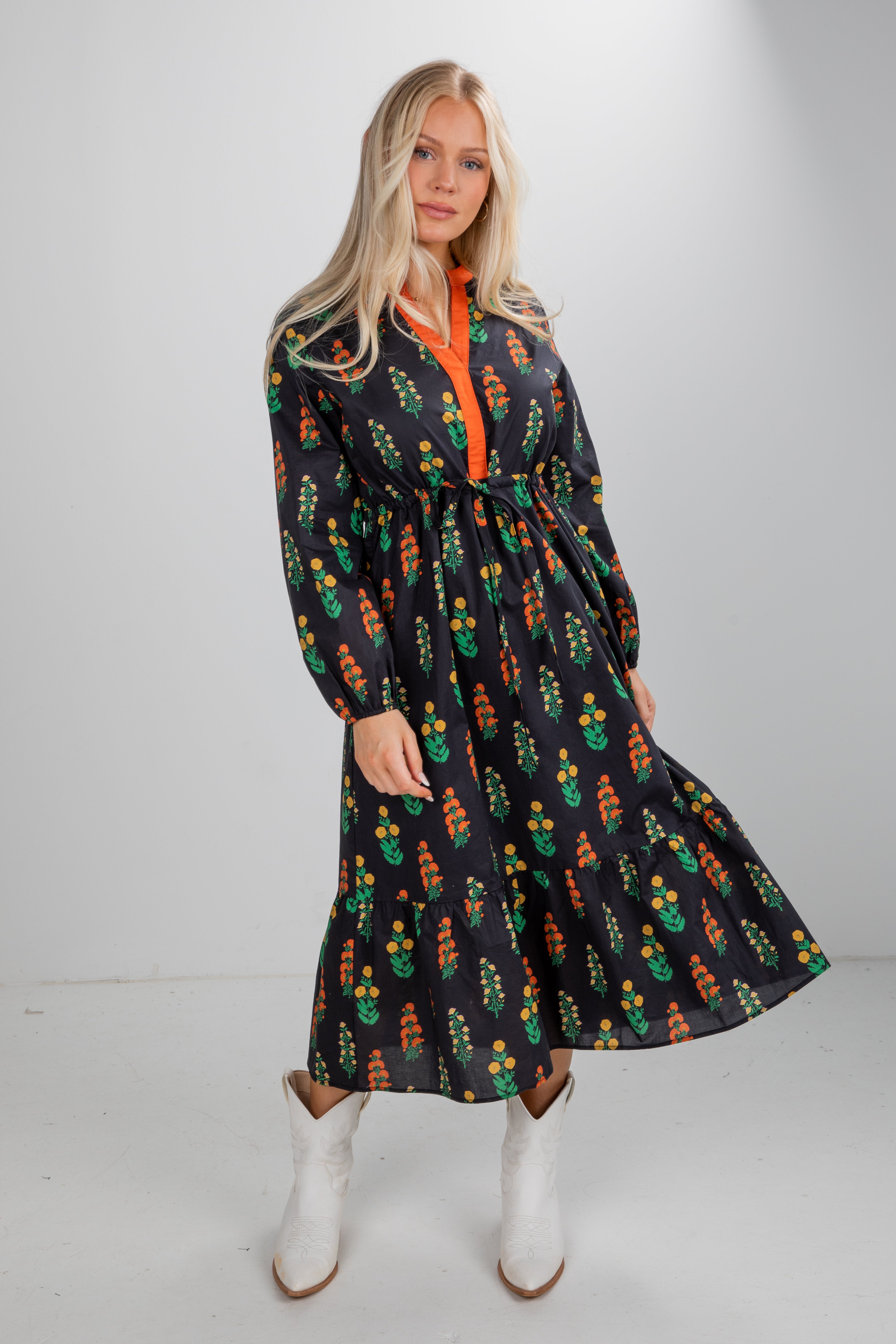 Woman wearing a black dress with colorful patterns and white boots on a plain background