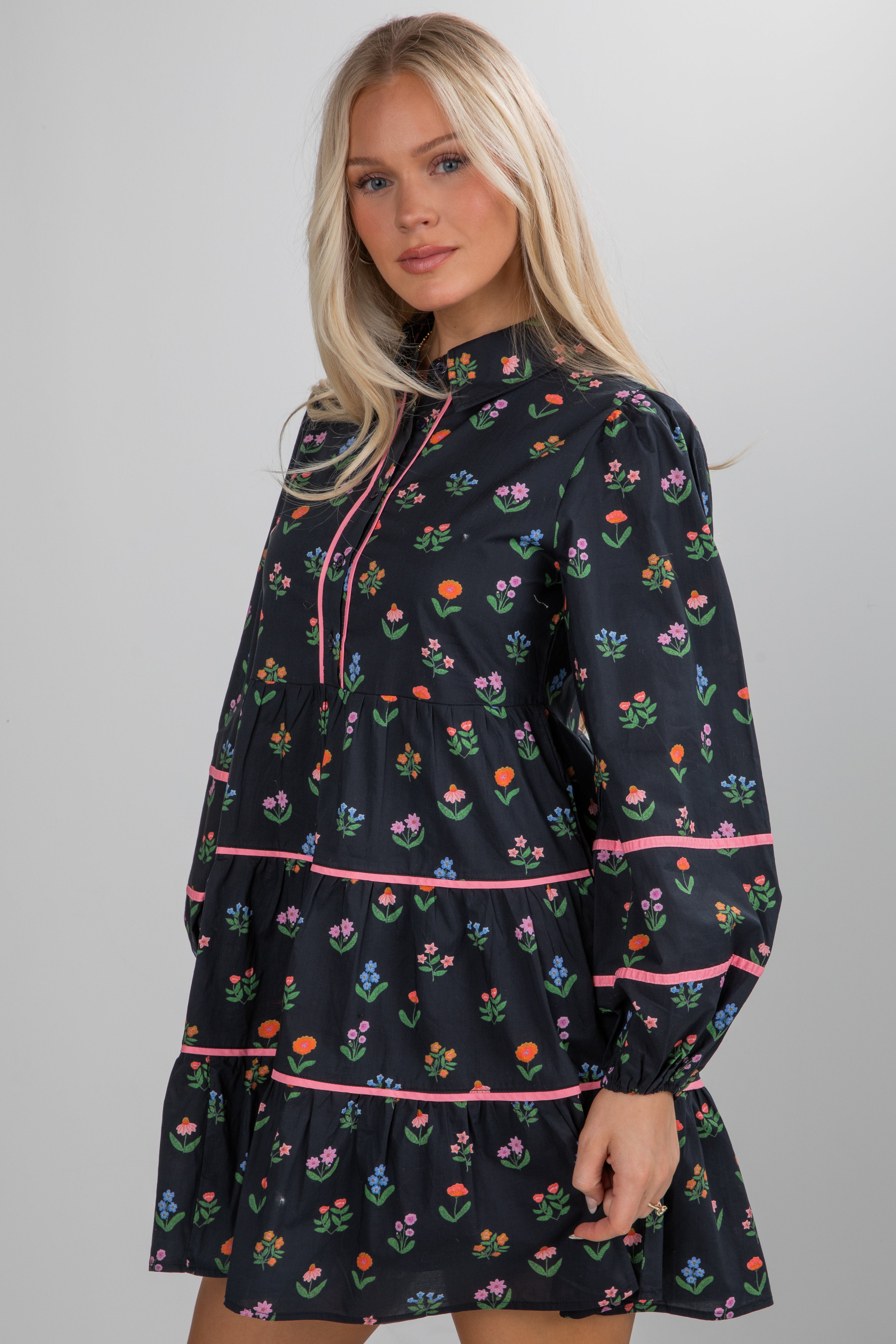 Woman wearing a black dress with floral pattern and pink trim on a gray background