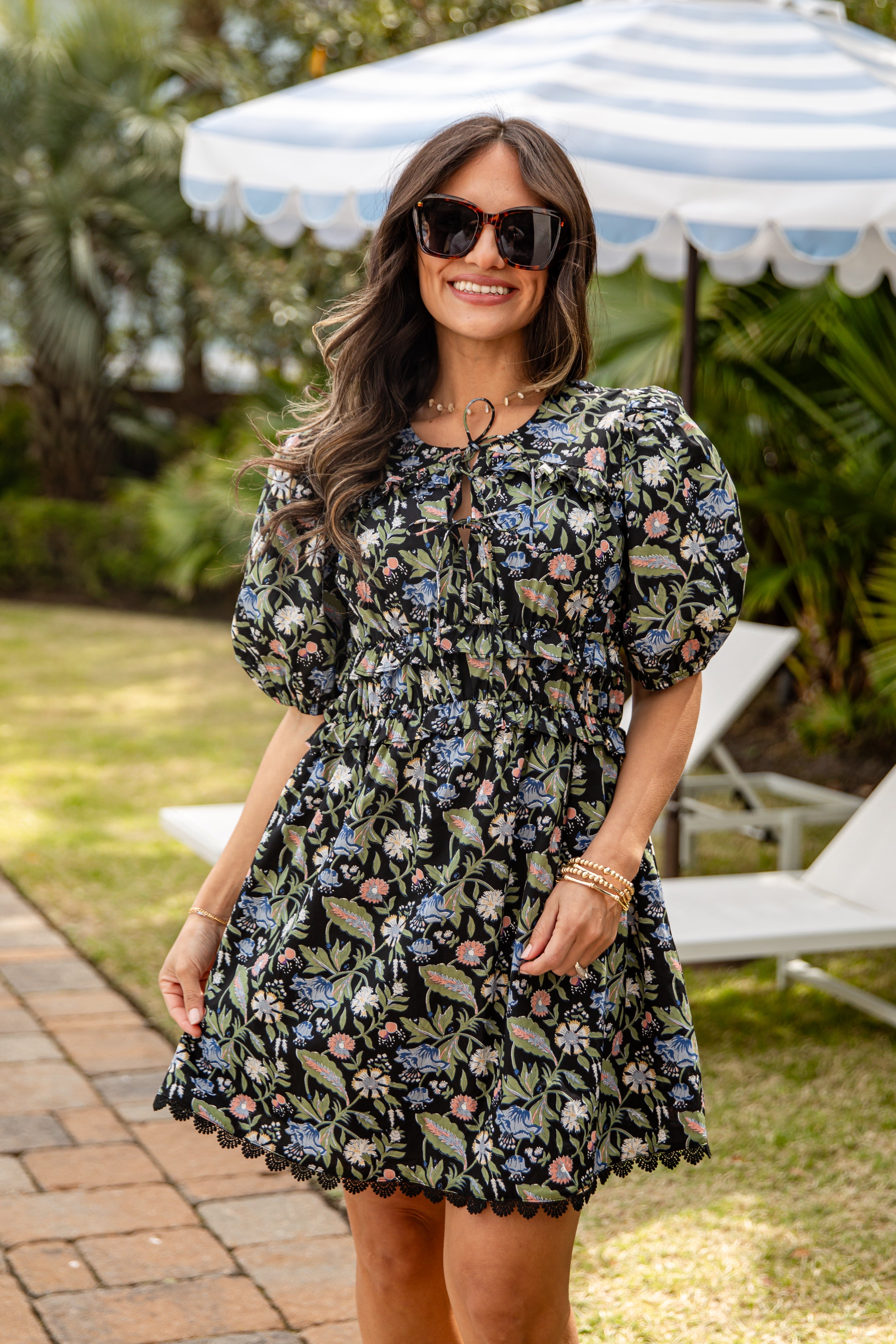 Woman wearing a floral dress standing outdoors under a striped umbrella.
