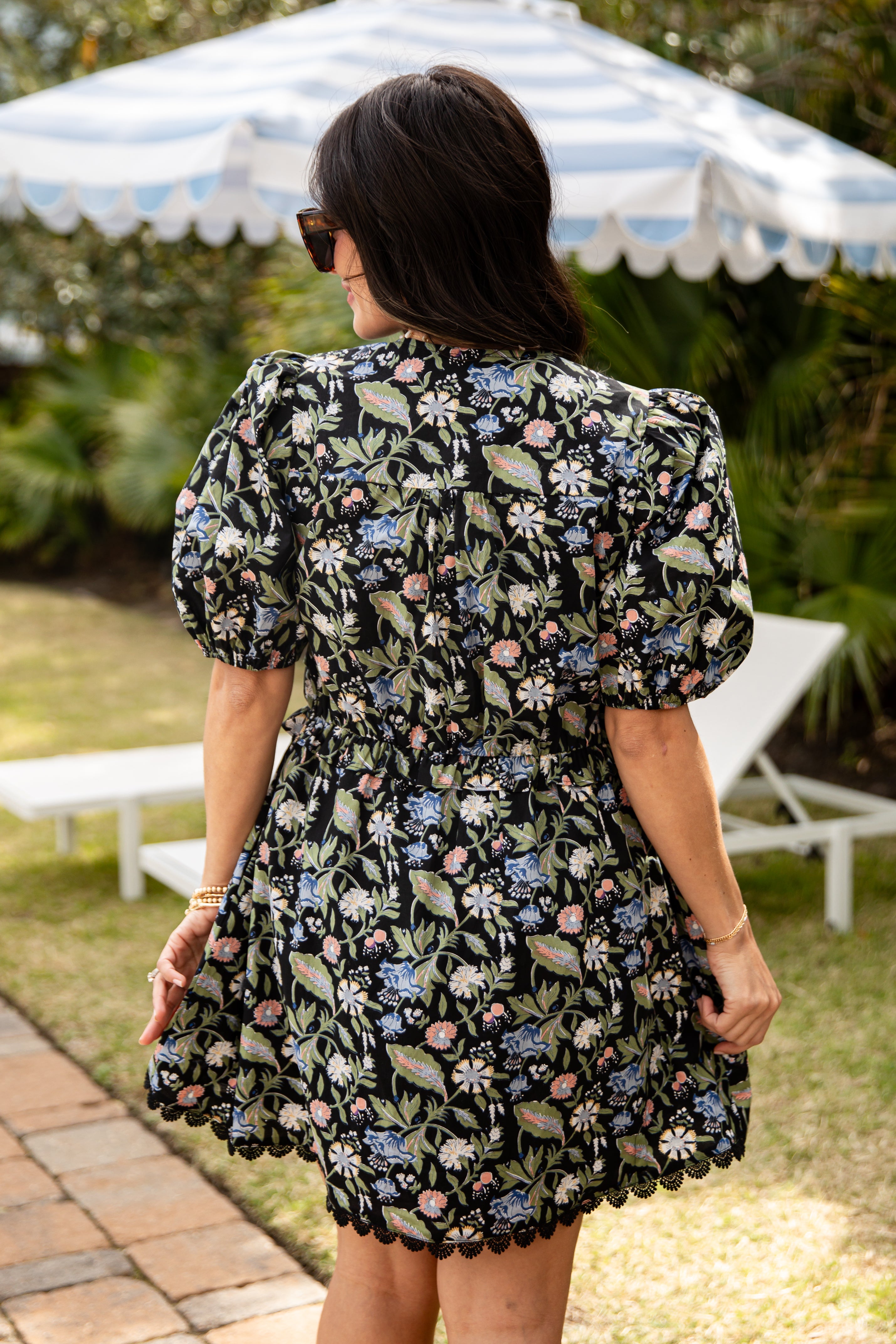 Woman wearing a floral dress in an outdoor setting with a striped umbrella.