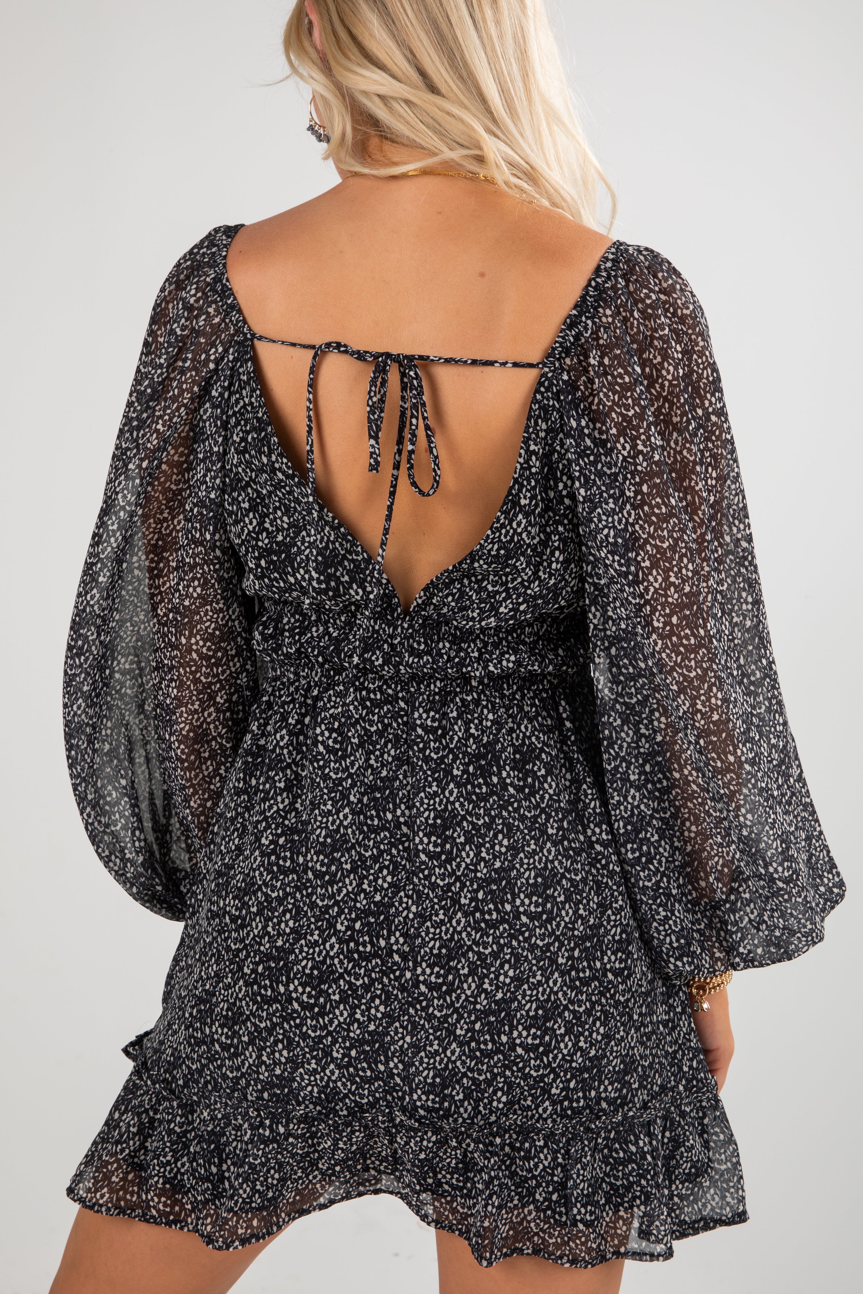 Black floral dress with sheer sleeves and open back on a plain background