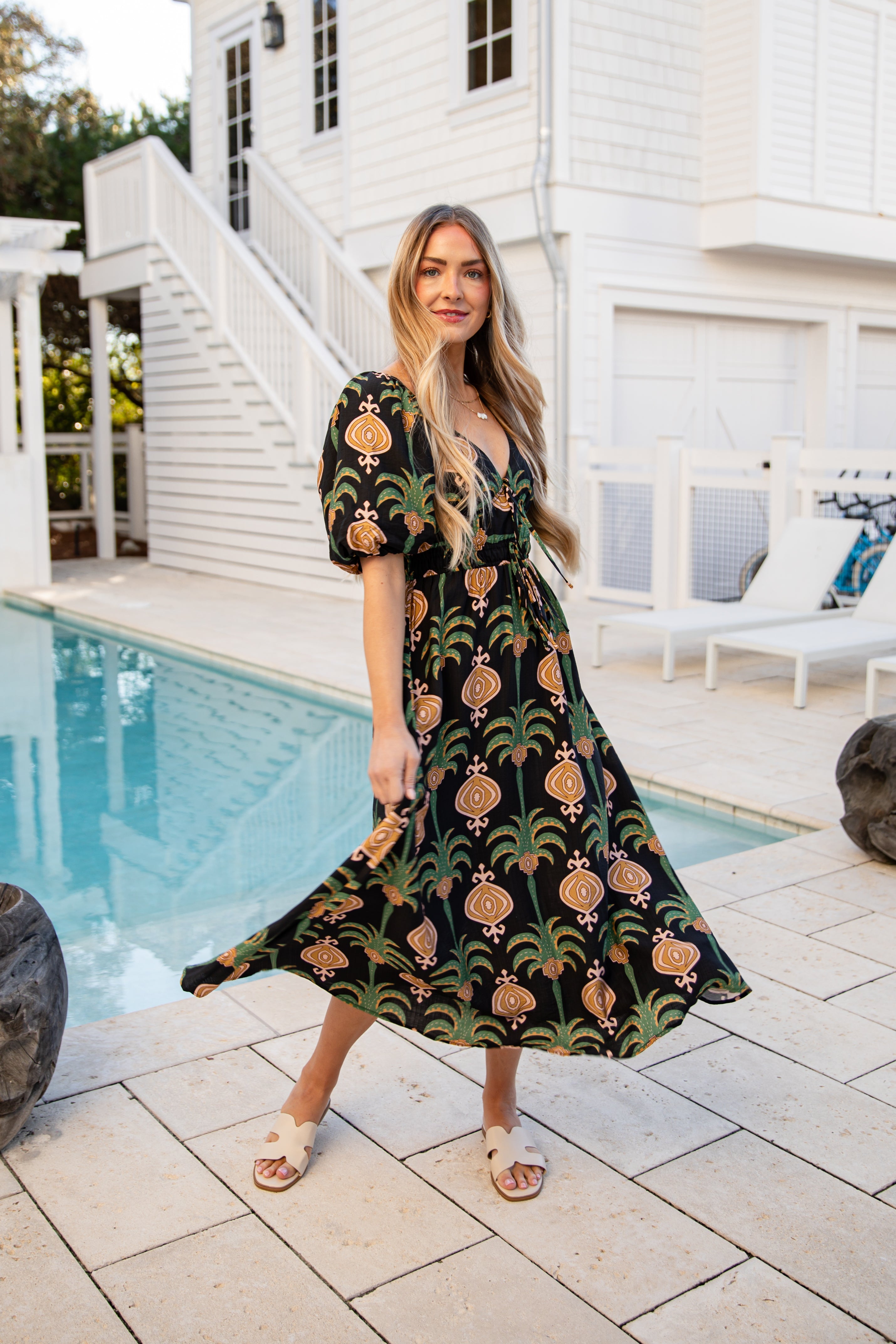 Woman in a patterned dress standing by a poolside.