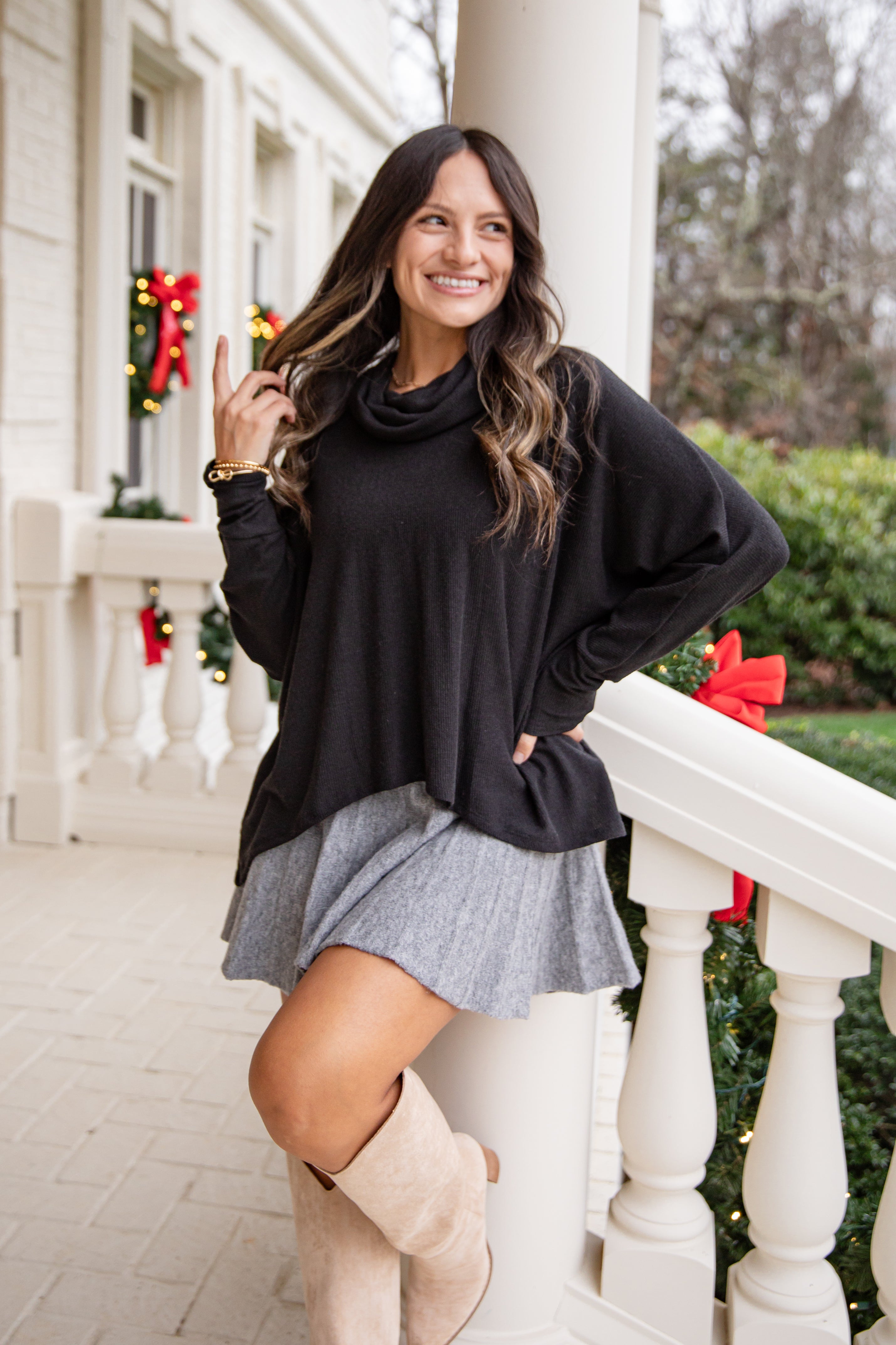 Woman in black sweater and gray skirt standing on a porch with Christmas decorations.