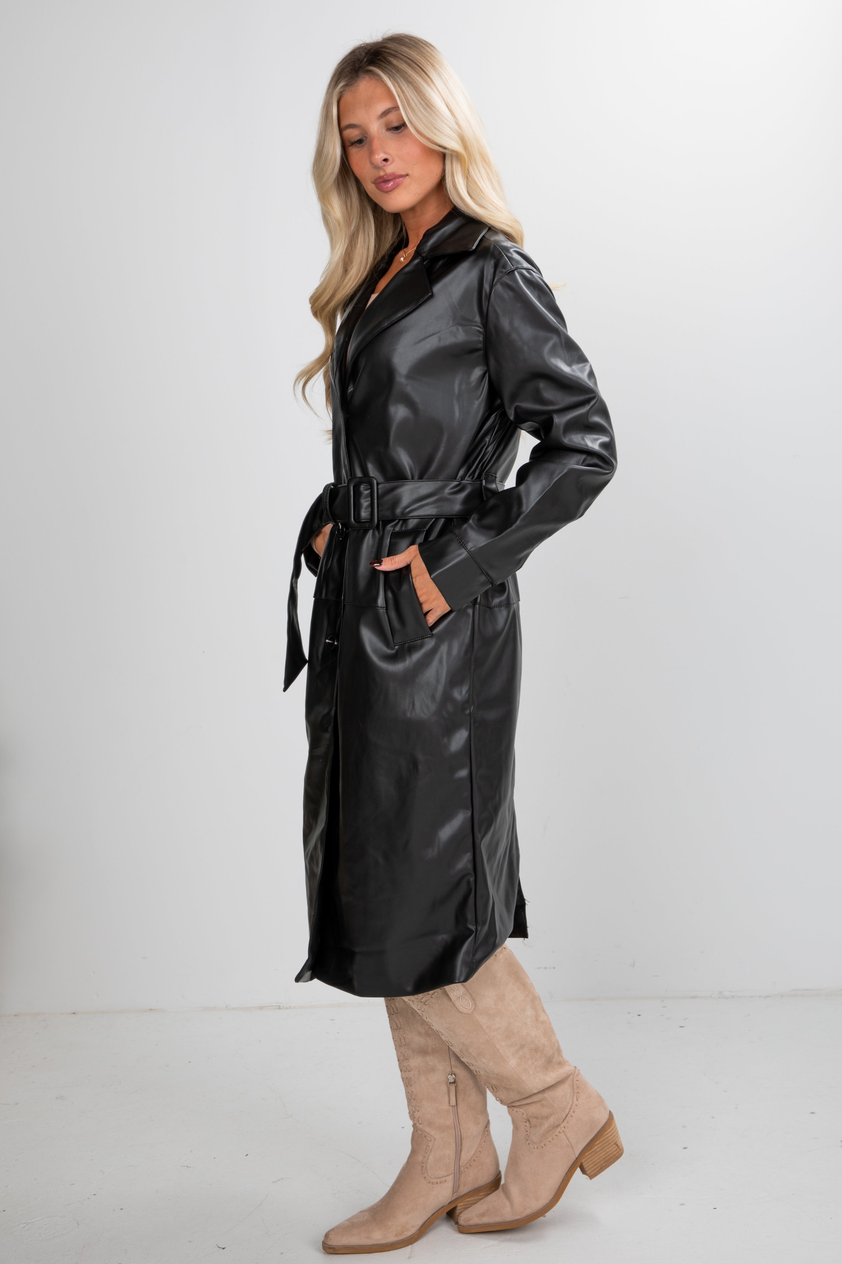 Woman wearing a black leather trench coat with beige boots on a white background
