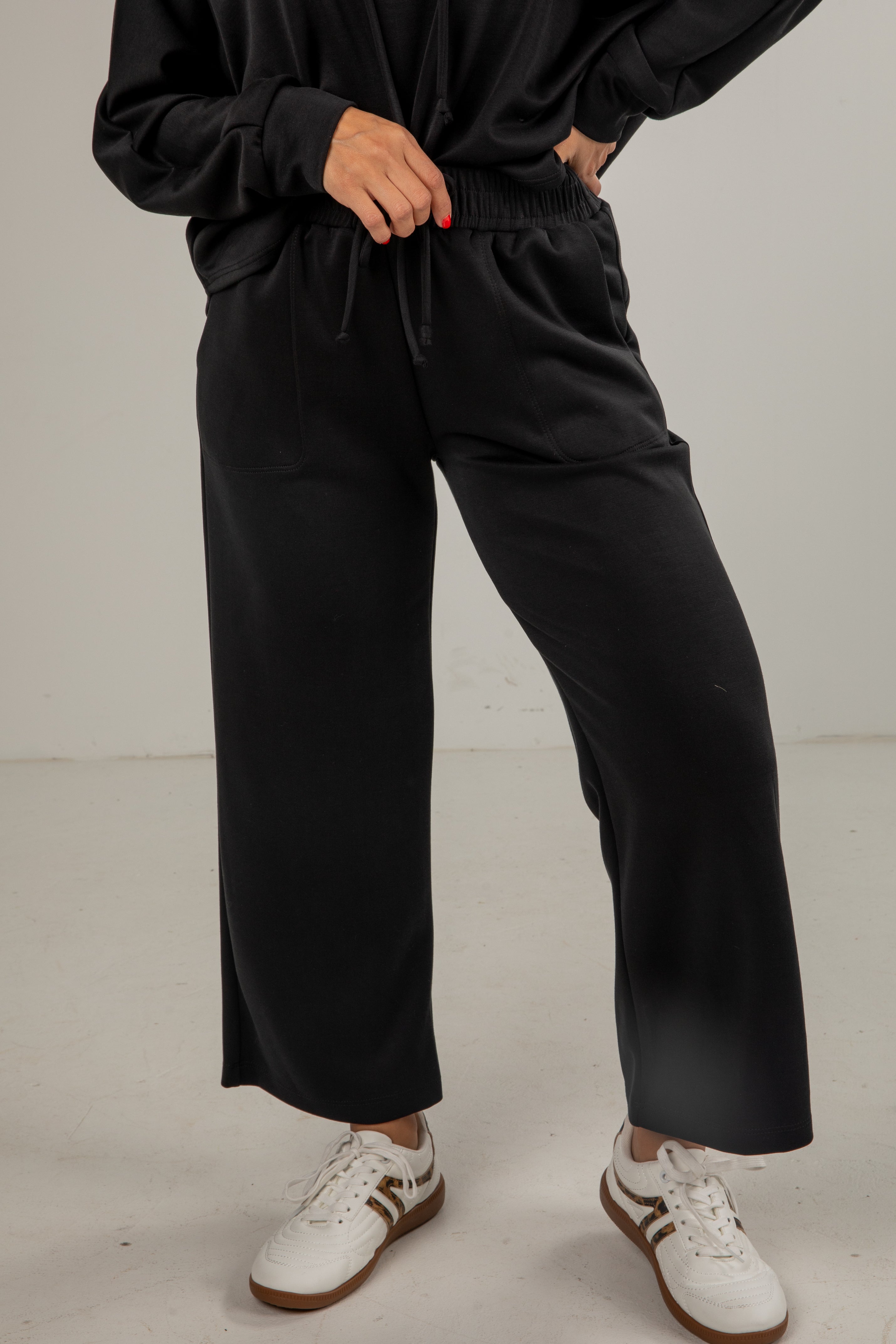 Person wearing black pants and white sneakers on a plain background