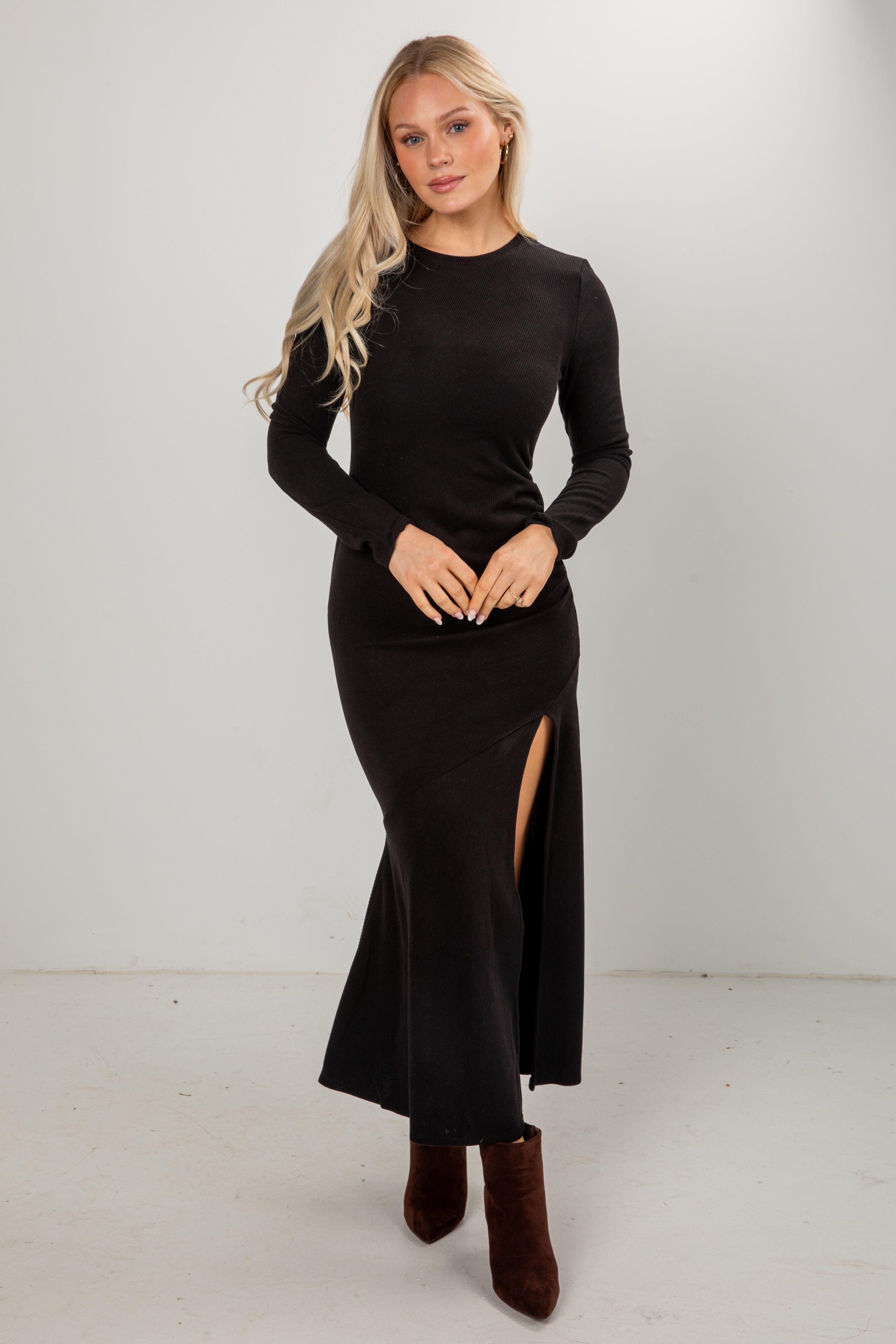 Woman wearing a black long-sleeve dress with a slit on a white background
