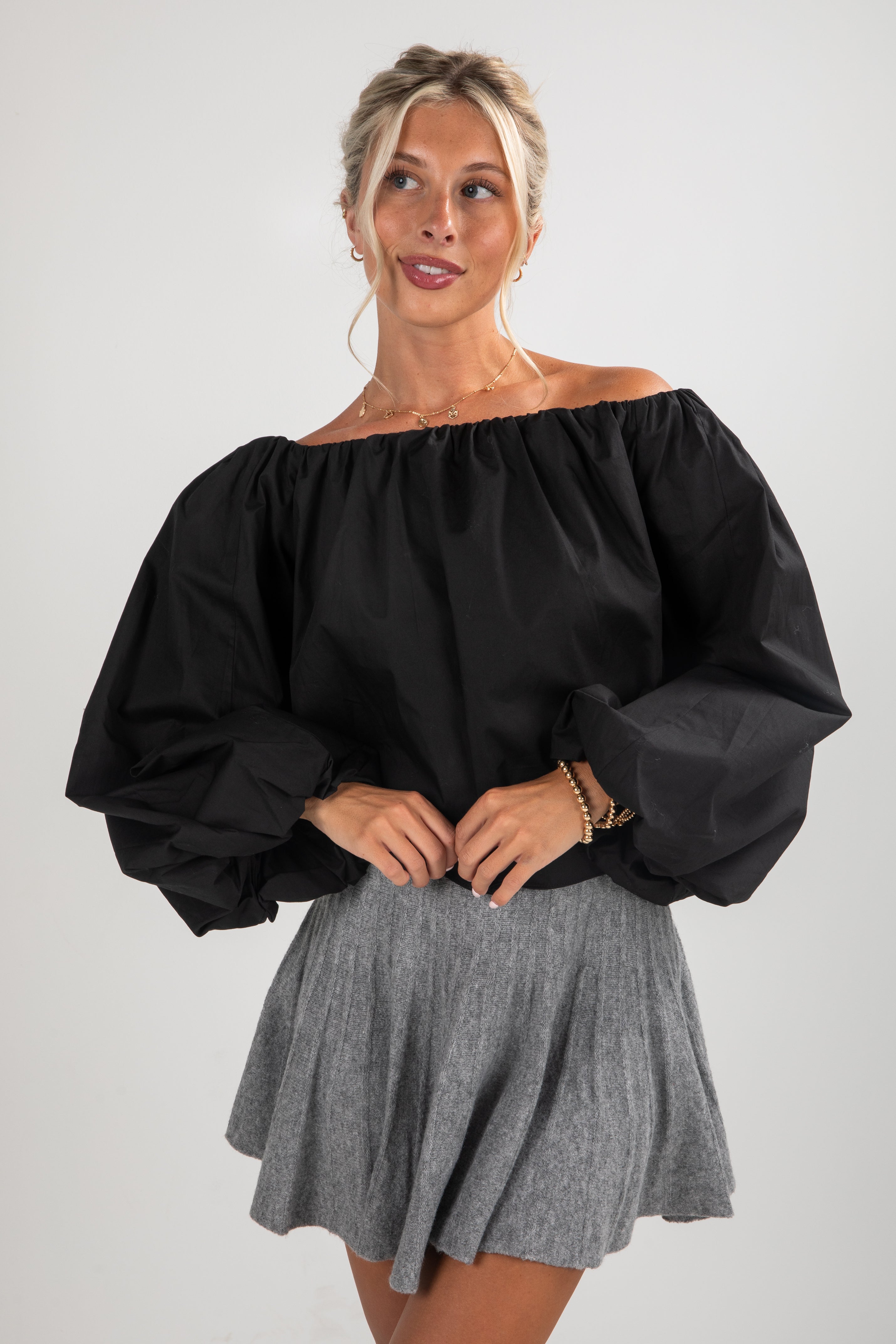 Woman wearing a black off-shoulder top and gray skirt on a white background