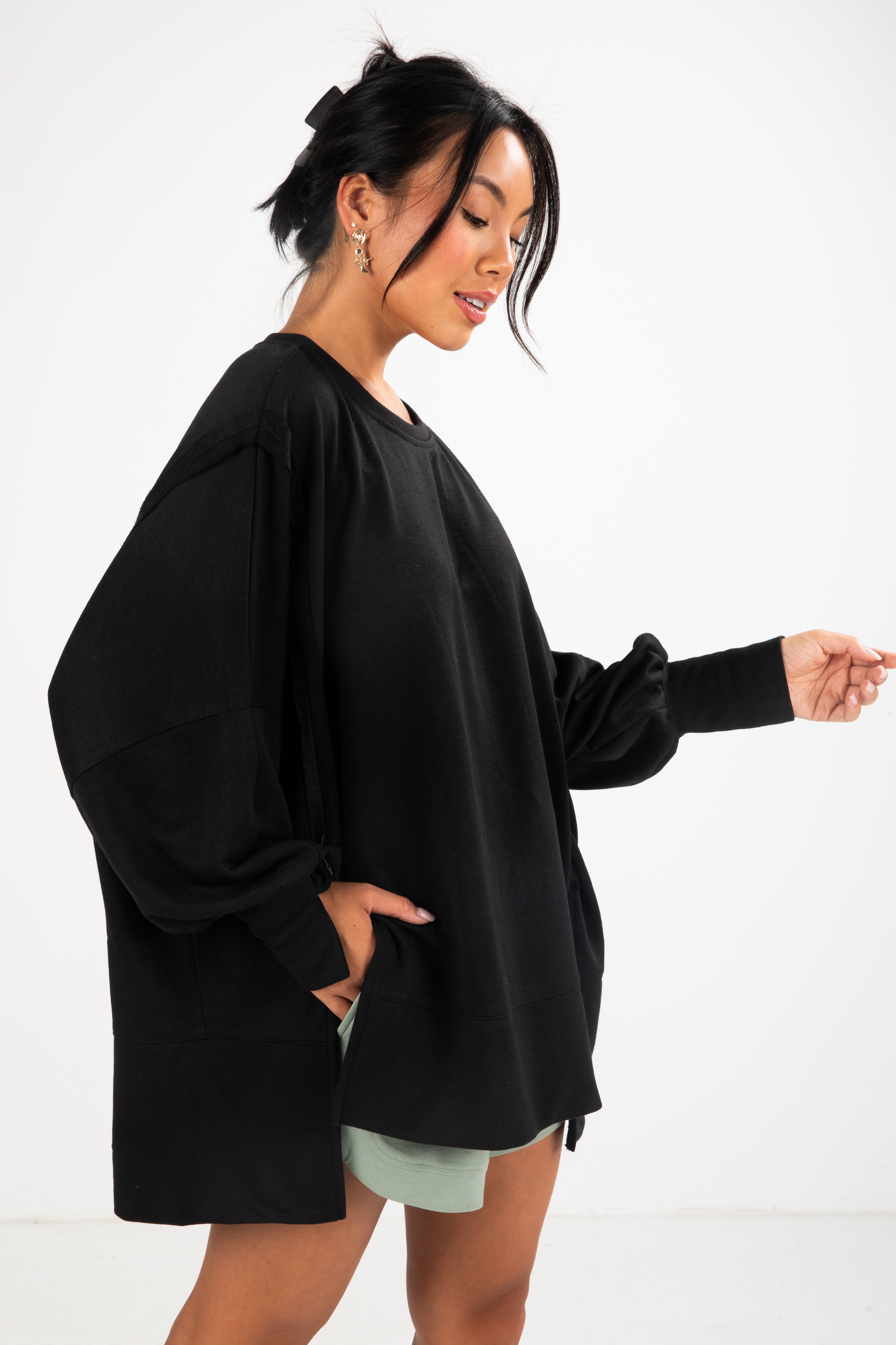 Woman wearing a black oversized sweater with light green shorts on a white background