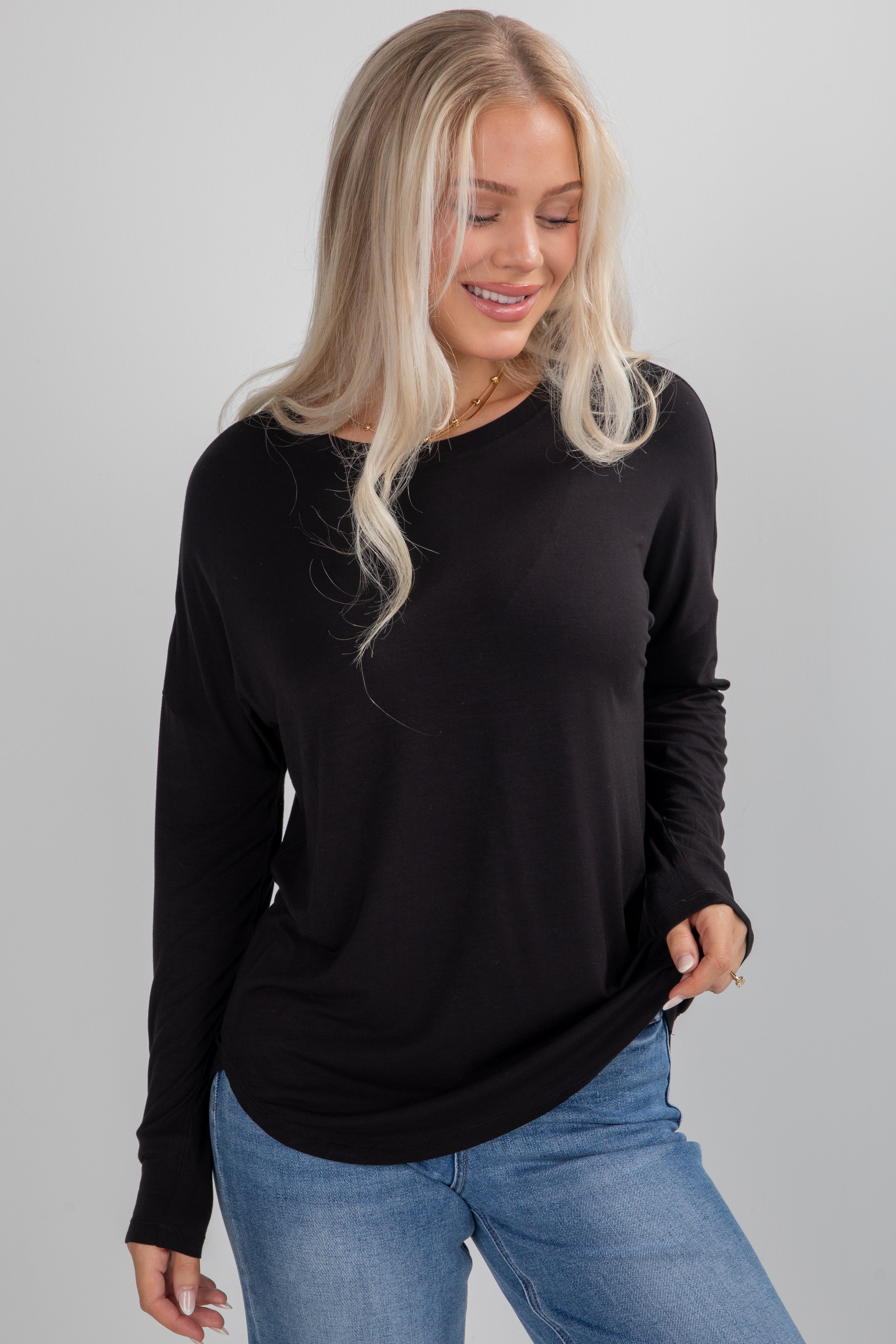 Woman wearing a black long-sleeve top and blue jeans against a gray background