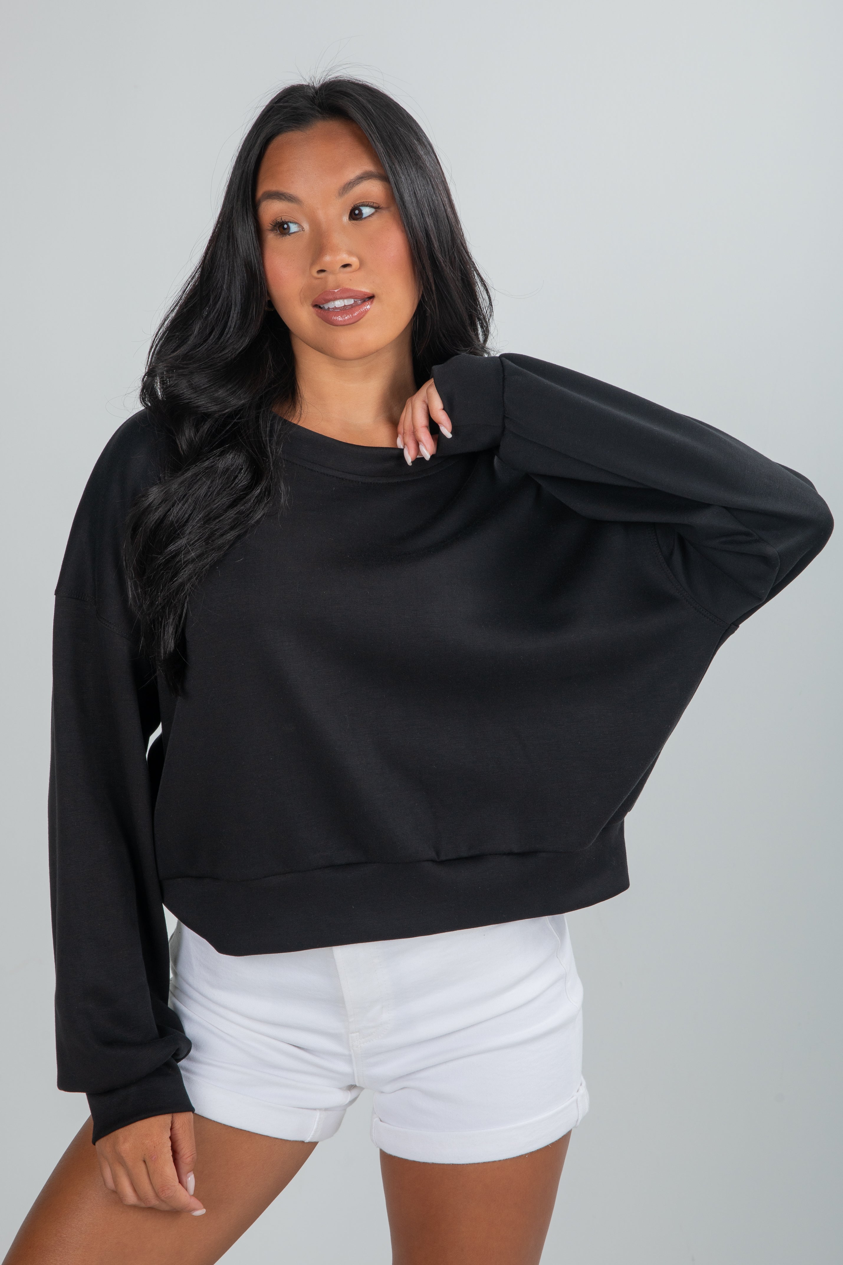 Woman wearing a black oversized sweater and white shorts on a gray background