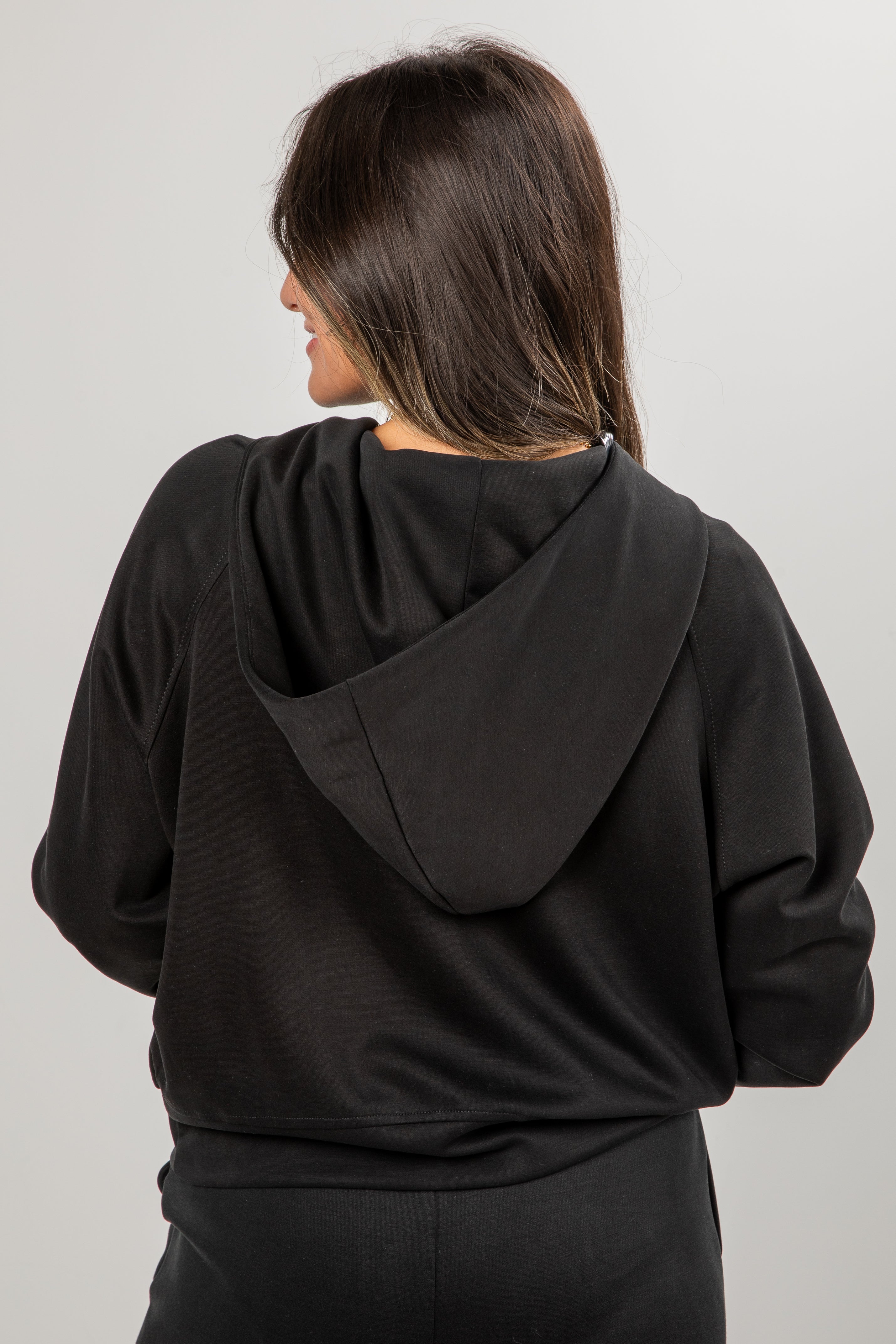 Person wearing a black hoodie from behind on a plain background