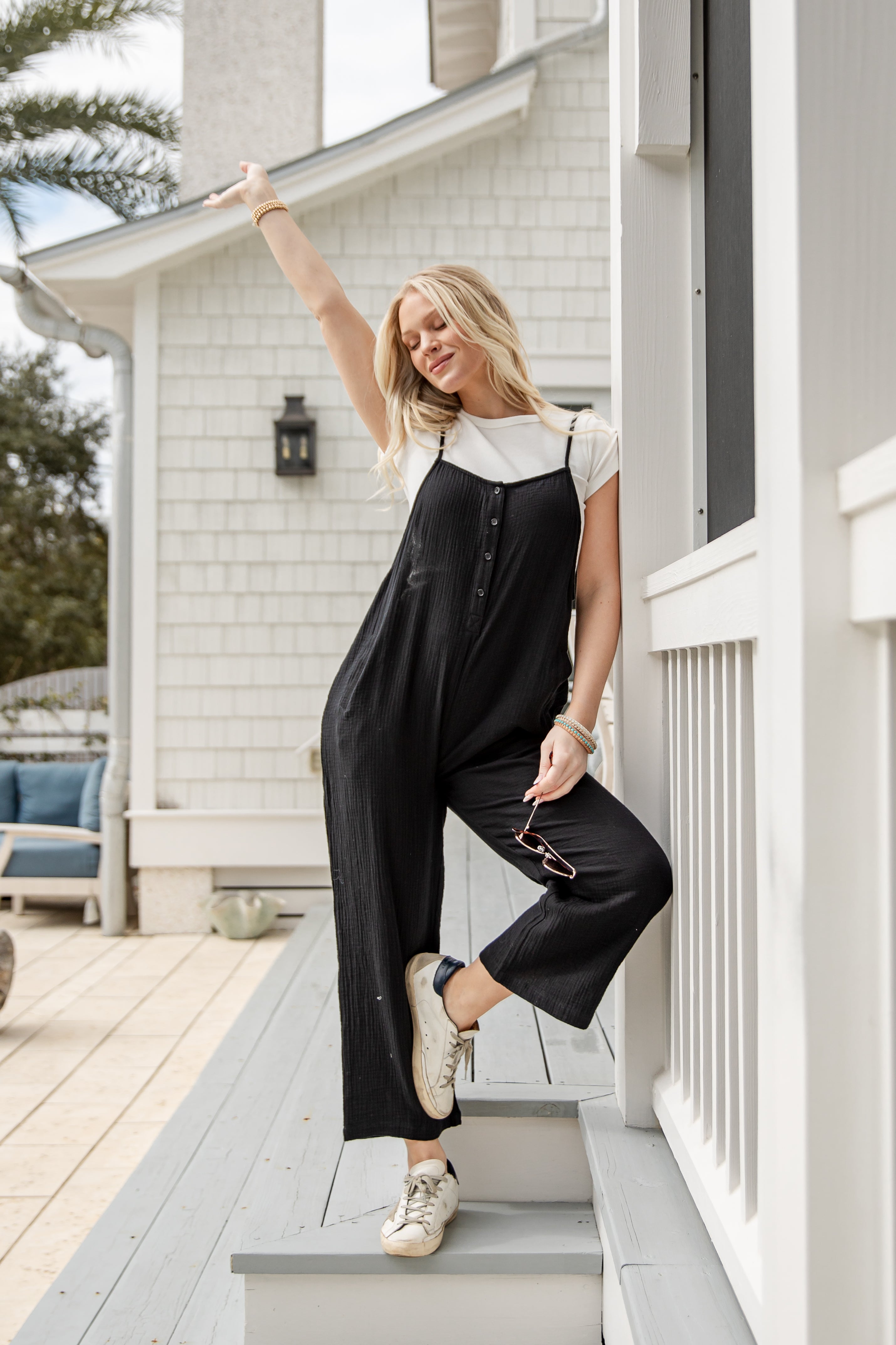 Woman in a black jumpsuit standing on a porch of a house.