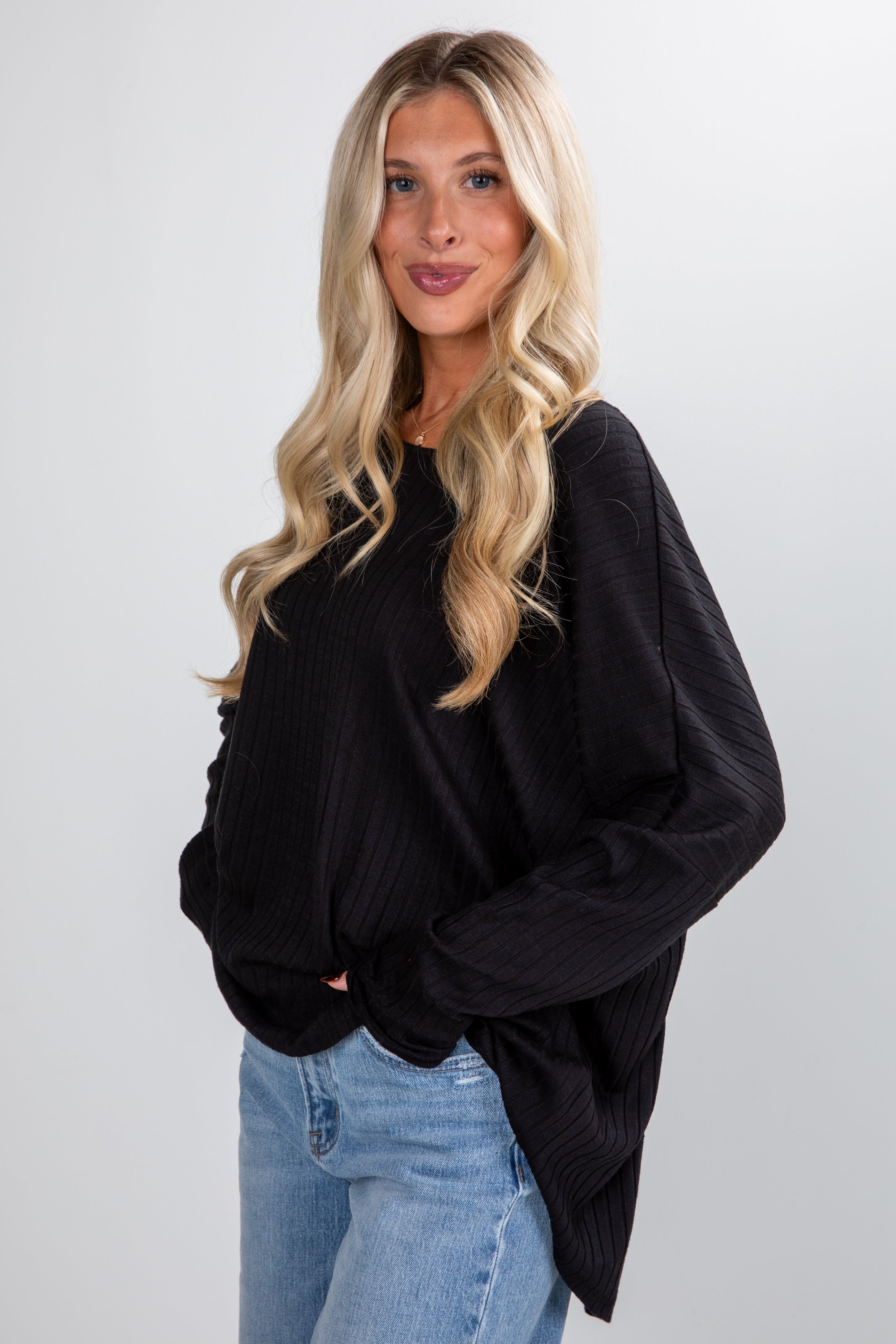 Woman wearing a black oversized sweater and blue jeans against a white background