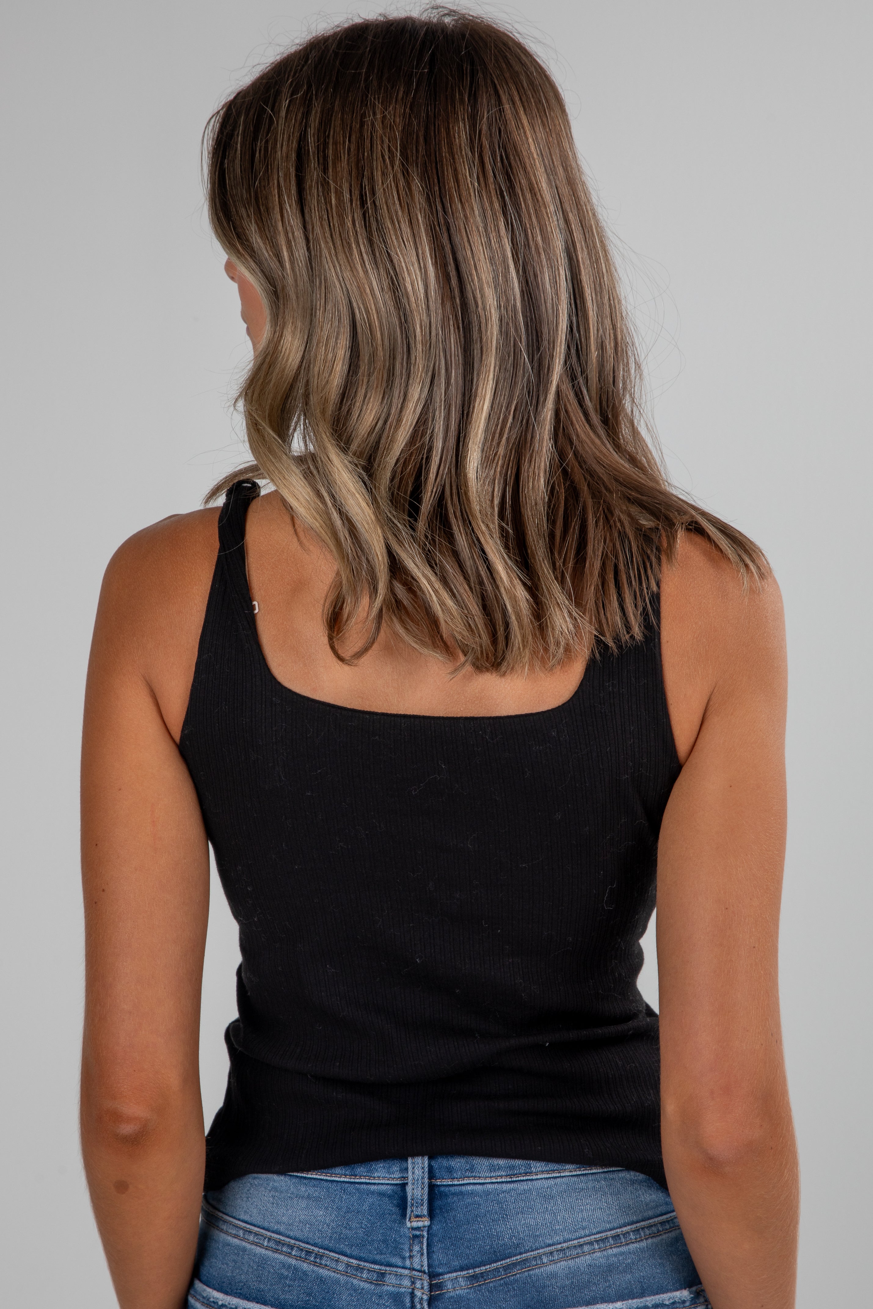 Person wearing a black tank top and blue jeans on a gray background