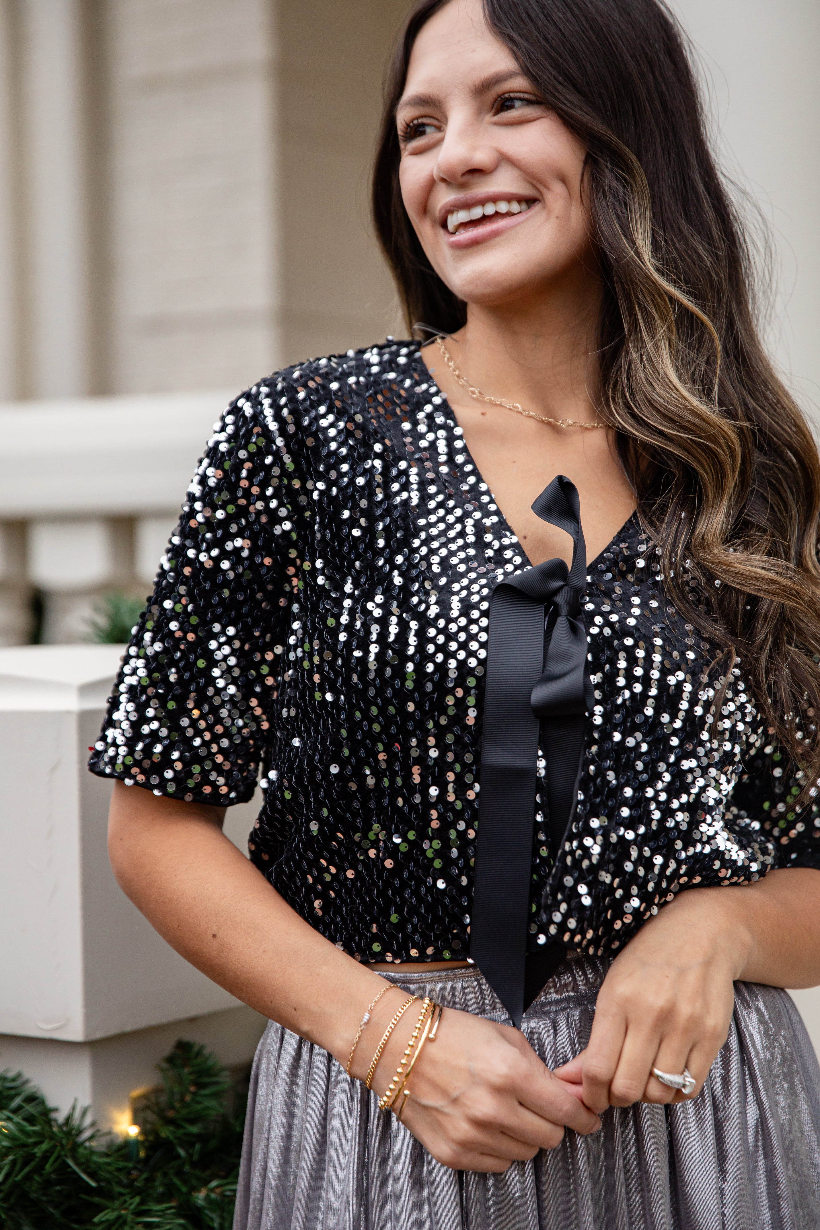Woman wearing a black sequin top with a bow and gray skirt outdoors.