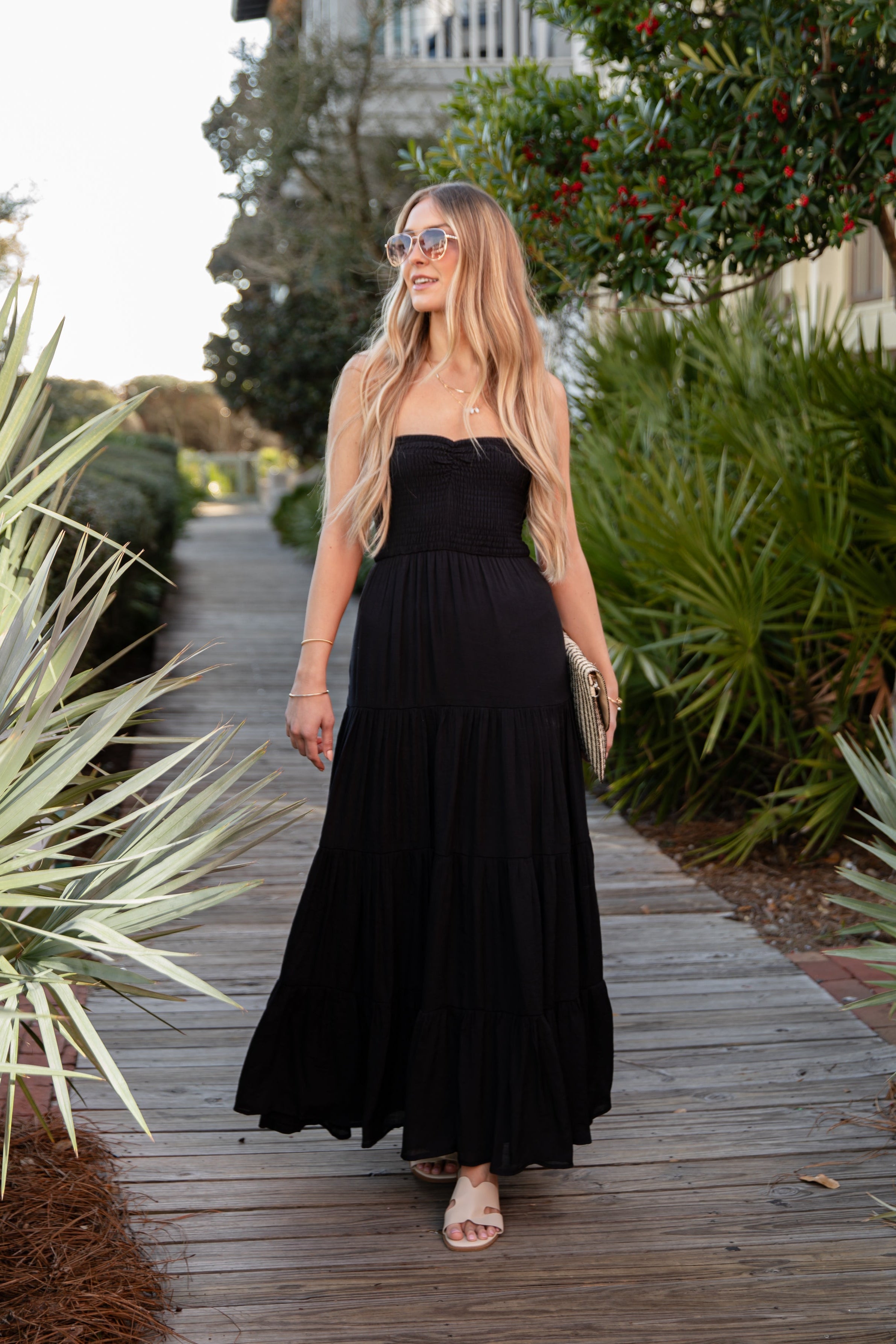 Woman in a black dress walking on a wooden path with greenery around.