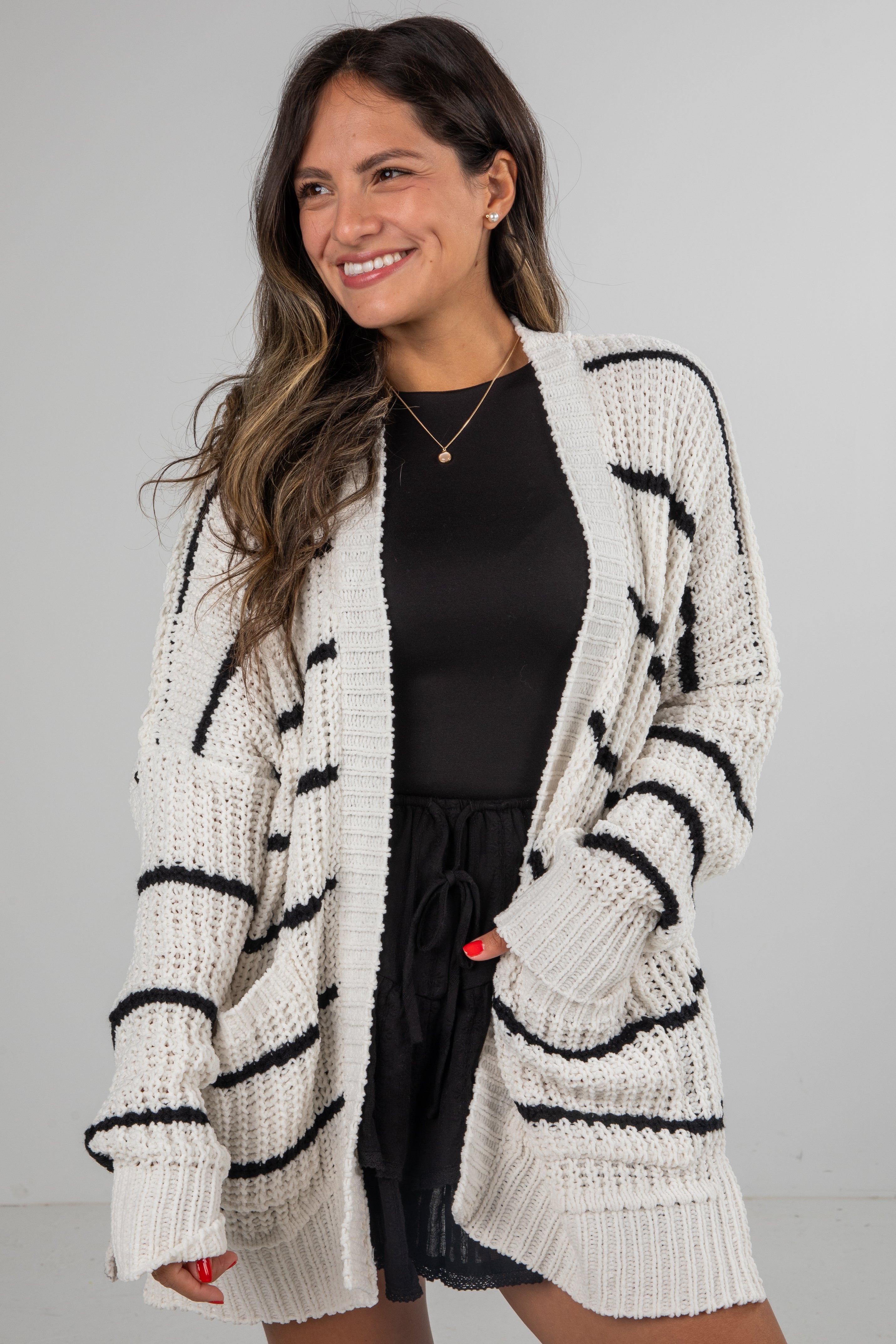 Woman wearing a white cardigan with black stripes on a gray background