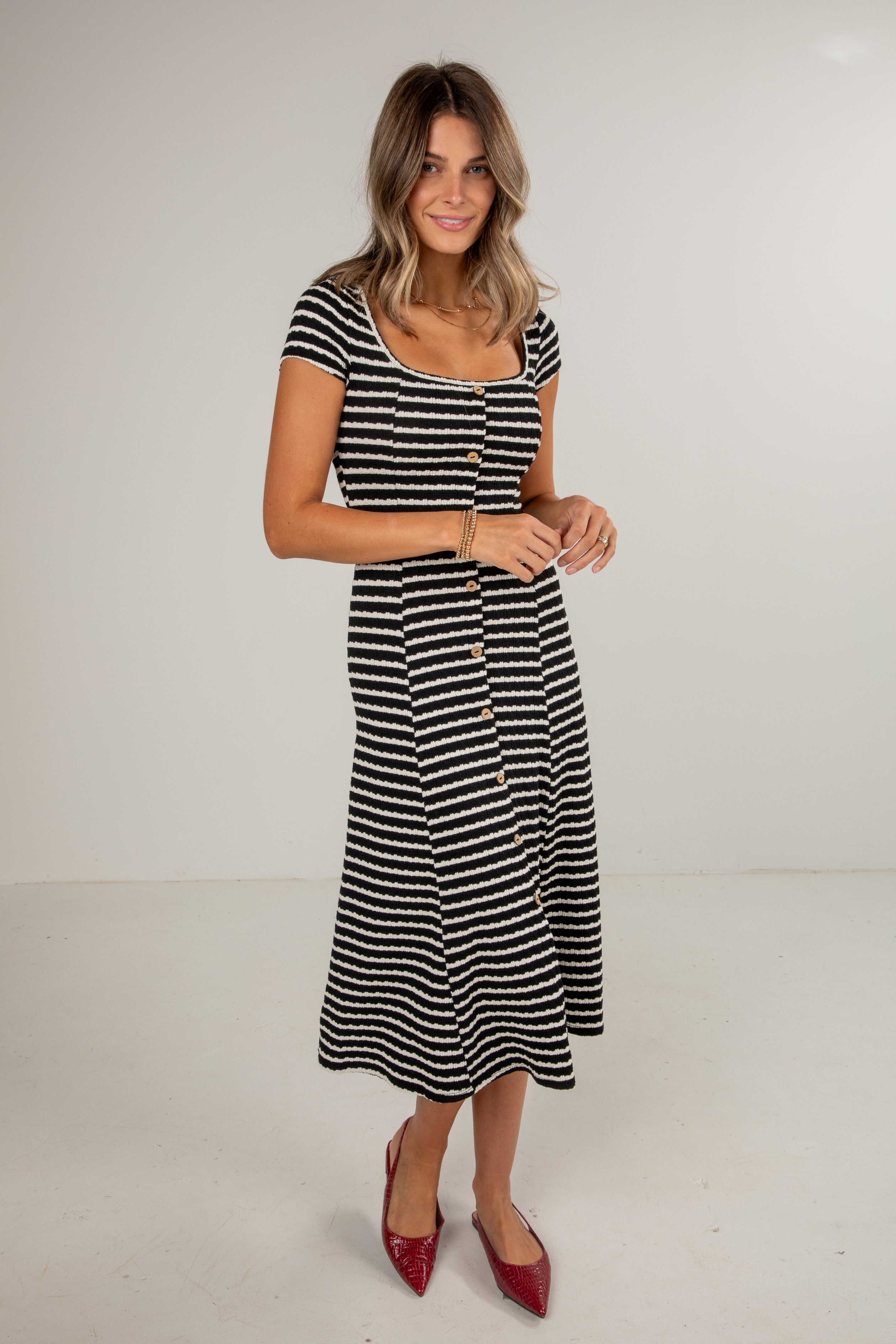 Woman wearing a black and white striped dress with red shoes on a plain background