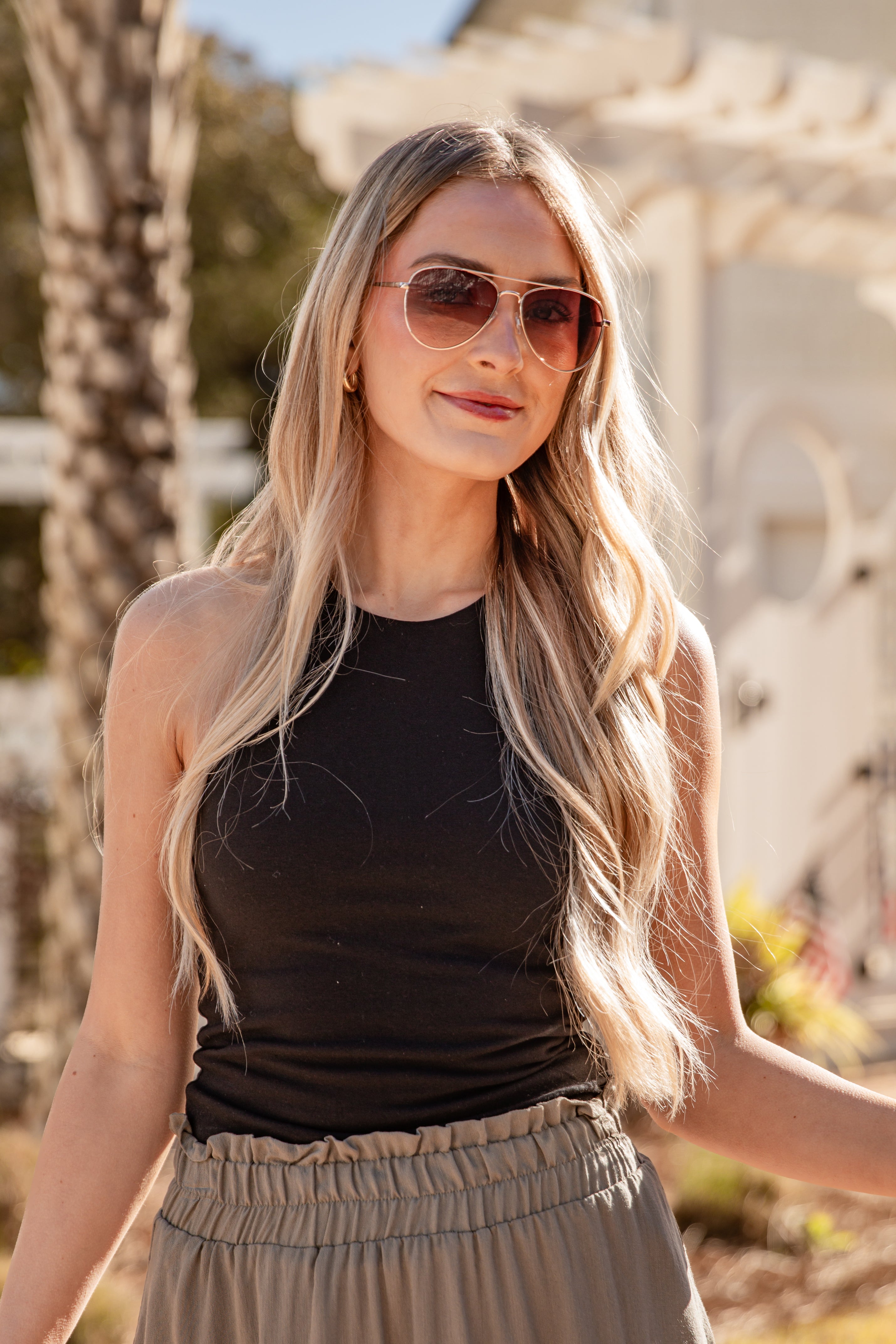 Woman wearing sunglasses and a black top with a blurred outdoor background