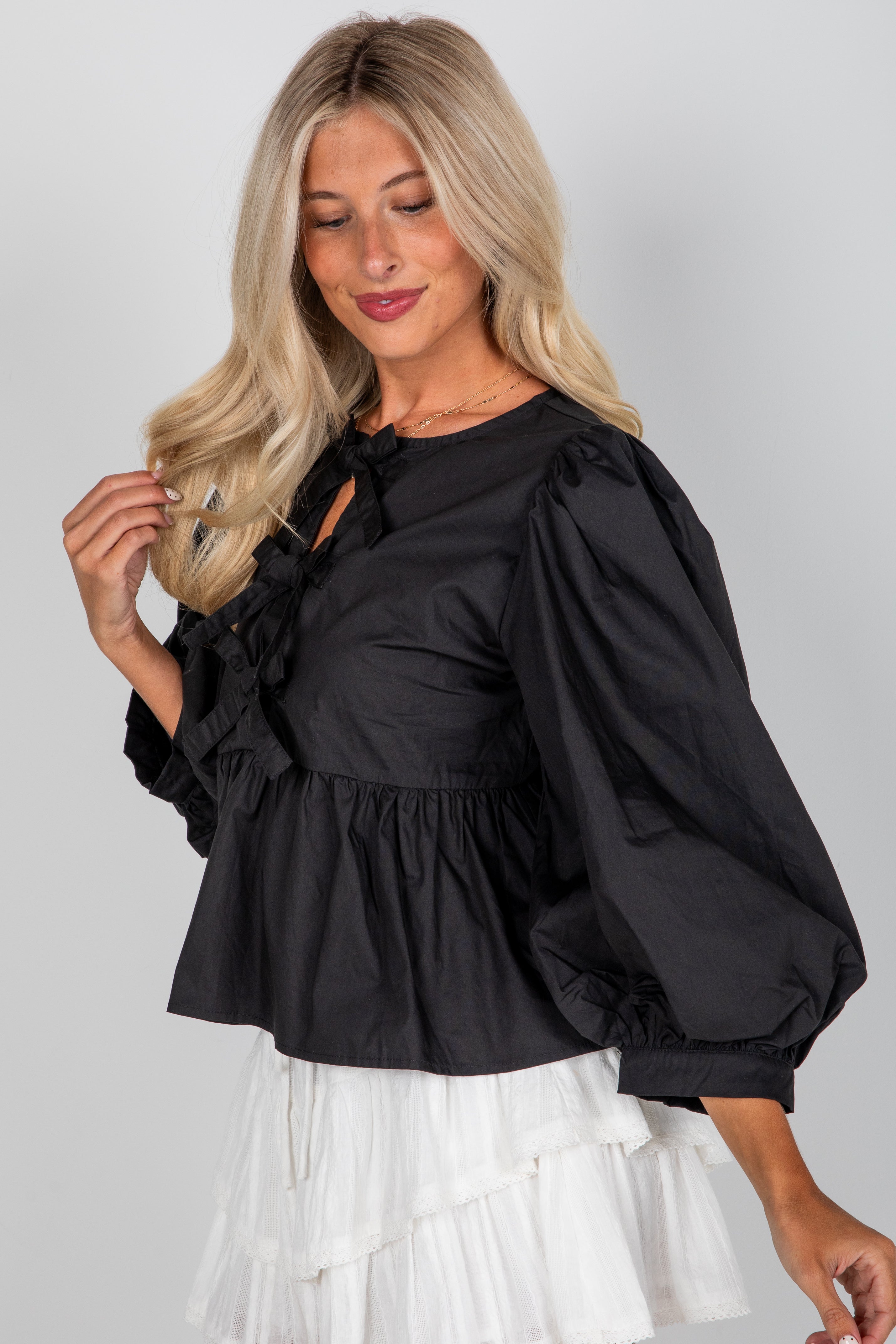 Woman wearing a black blouse with long sleeves and a white skirt on a plain background