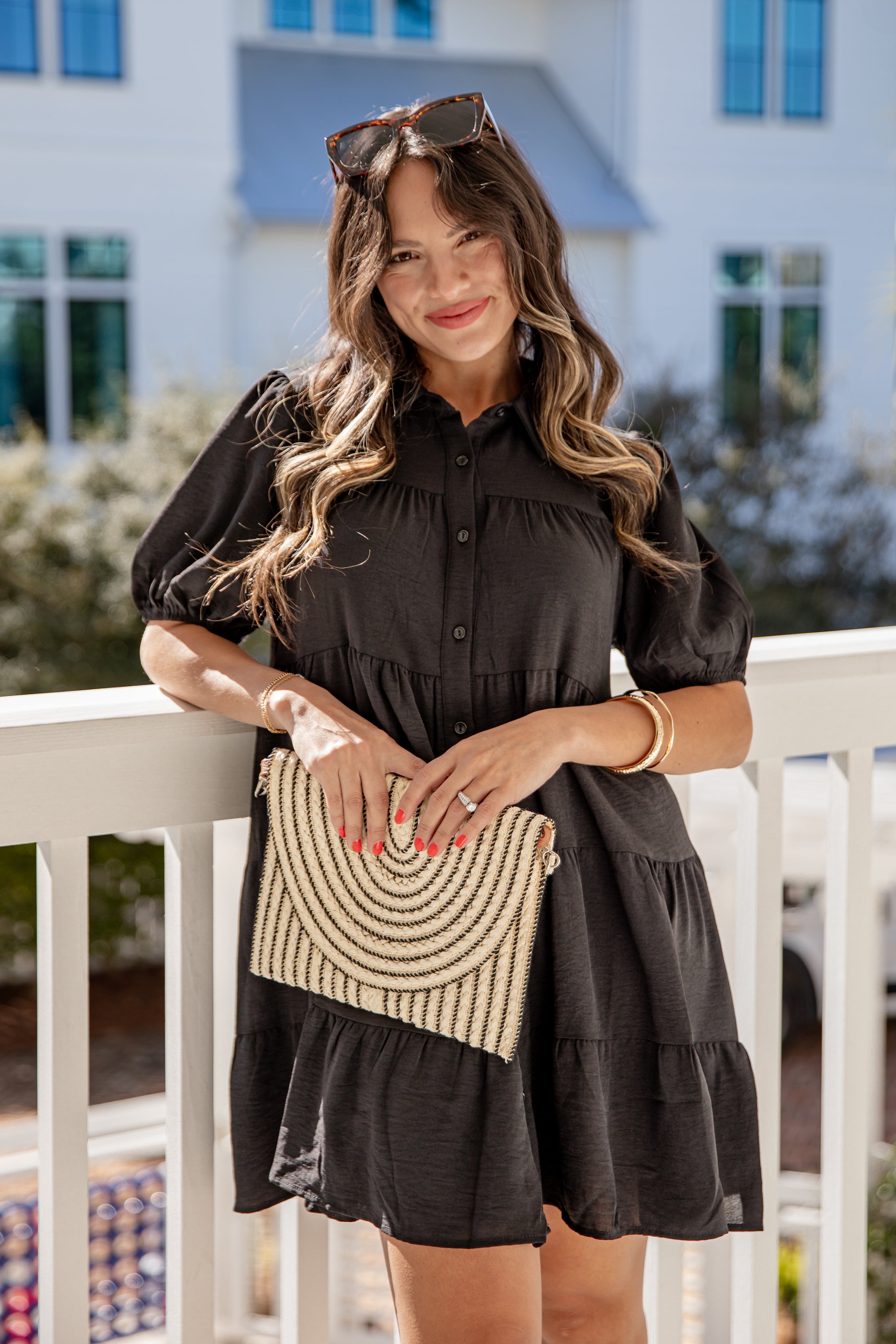Woman in a black dress holding a beaded handbag on a balcony.