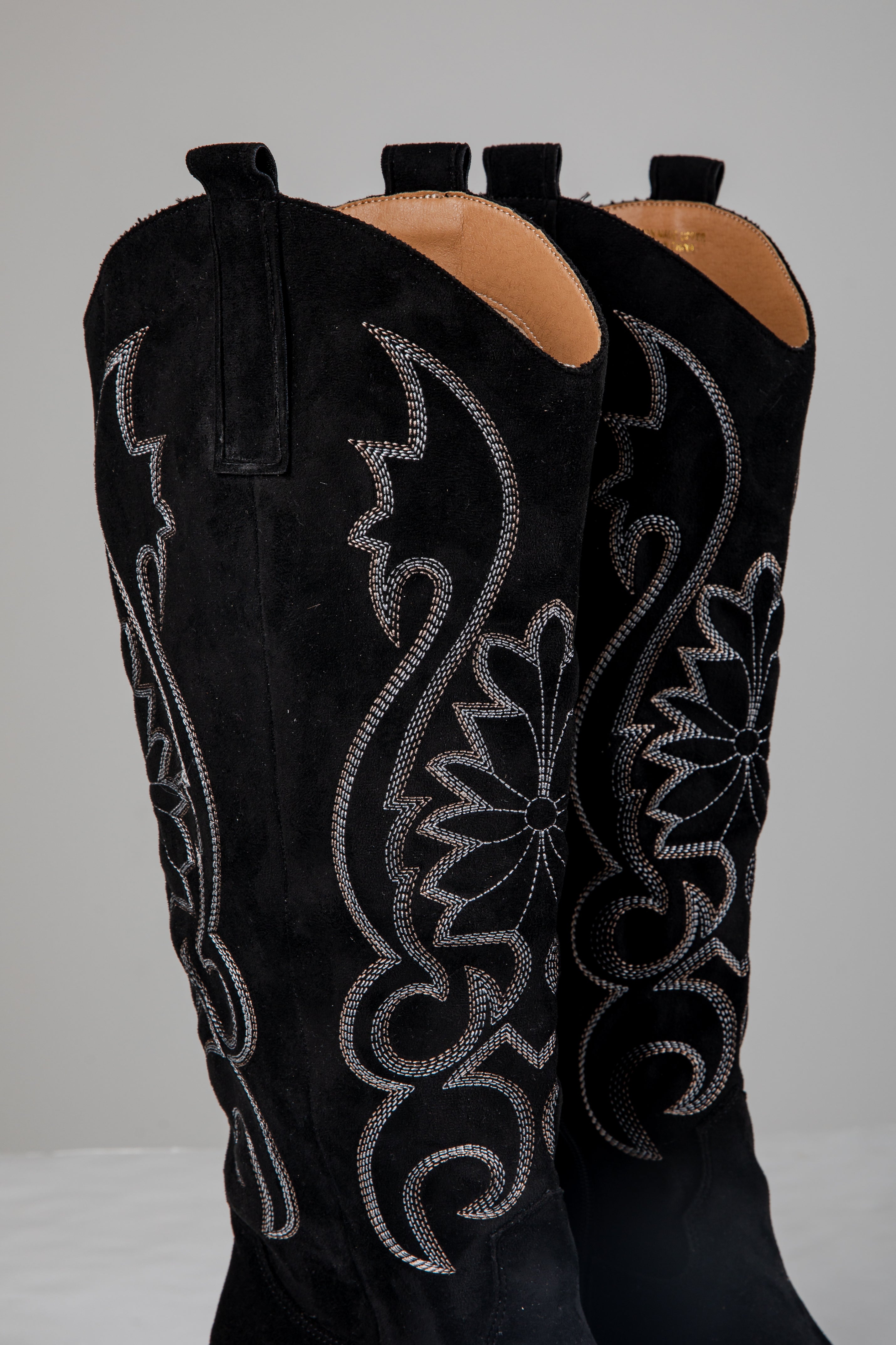 Black cowboy boots with intricate silver embroidery on a white background