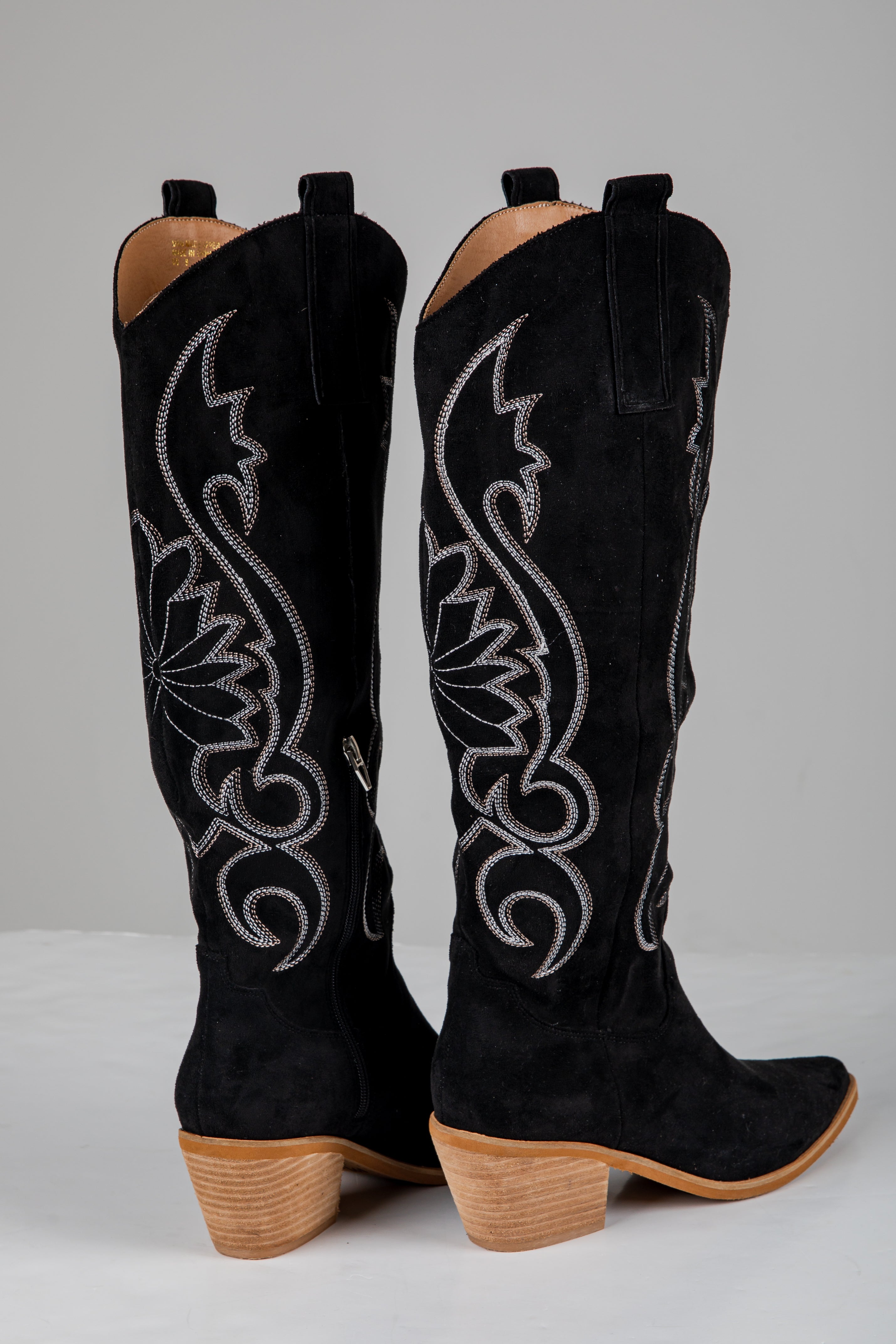 Black cowboy boots with intricate white embroidery on a gray background