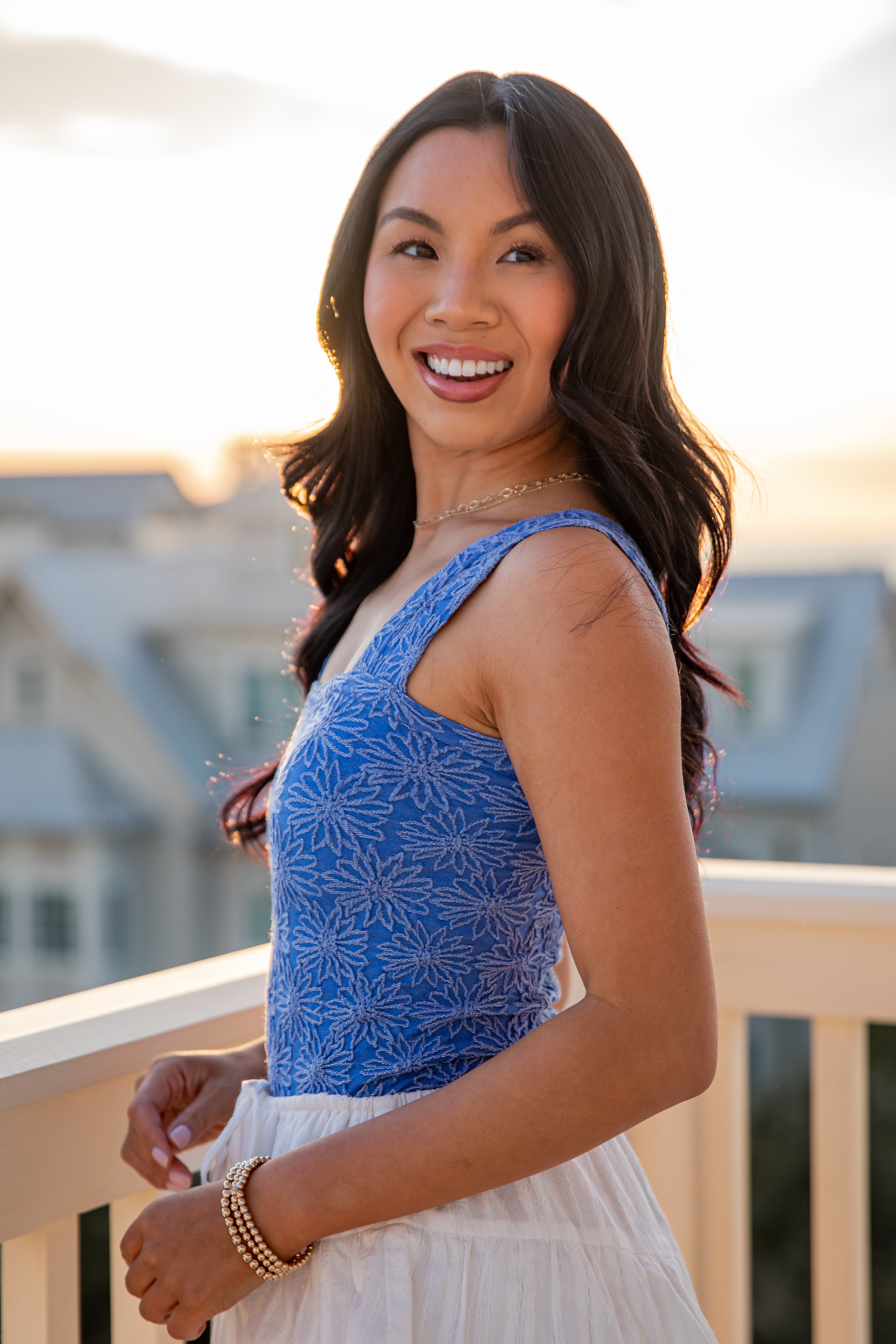 Woman wearing a blue top and white skirt on a balcony with a blurred background