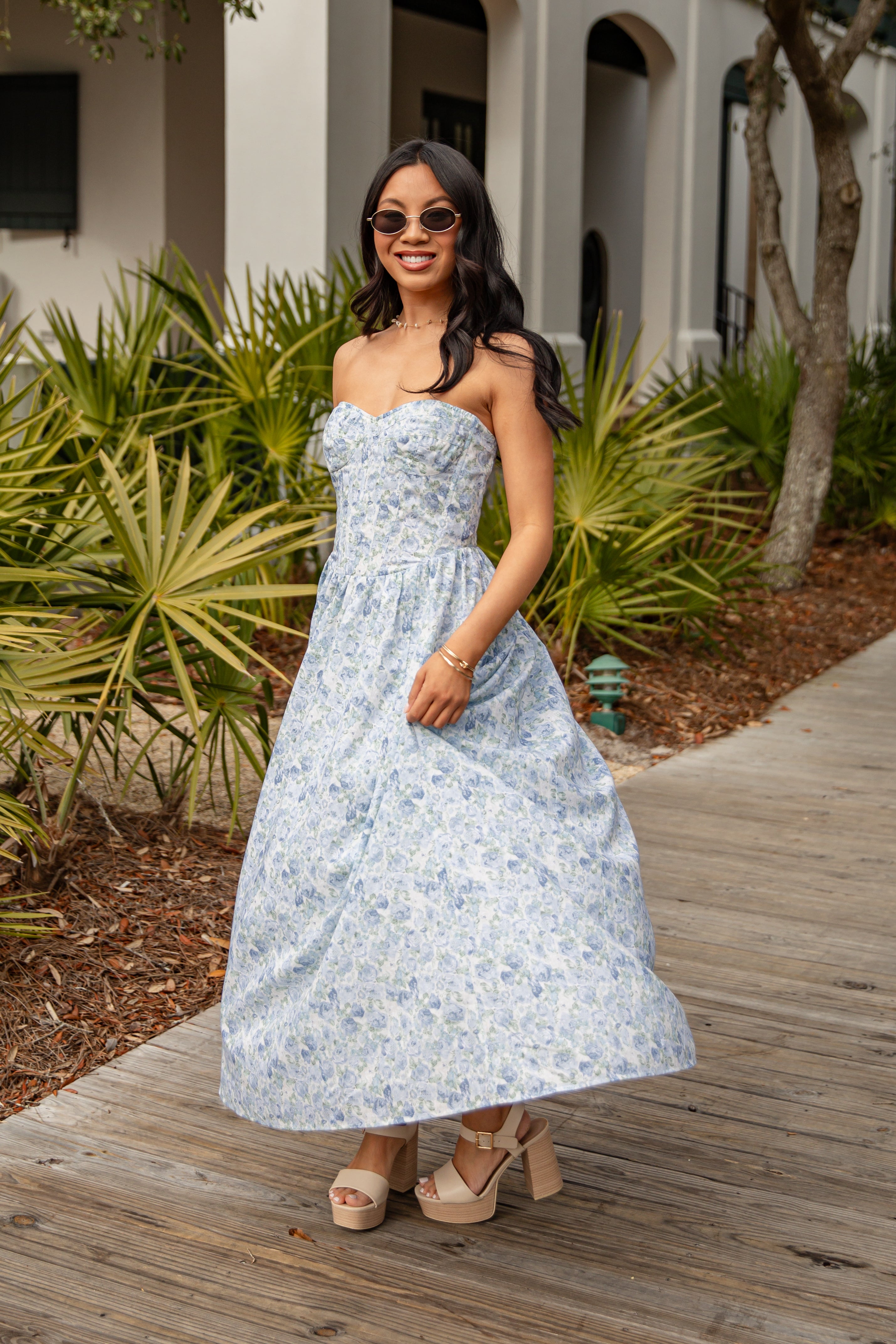 Woman in a floral dress standing on a wooden path with plants in the background