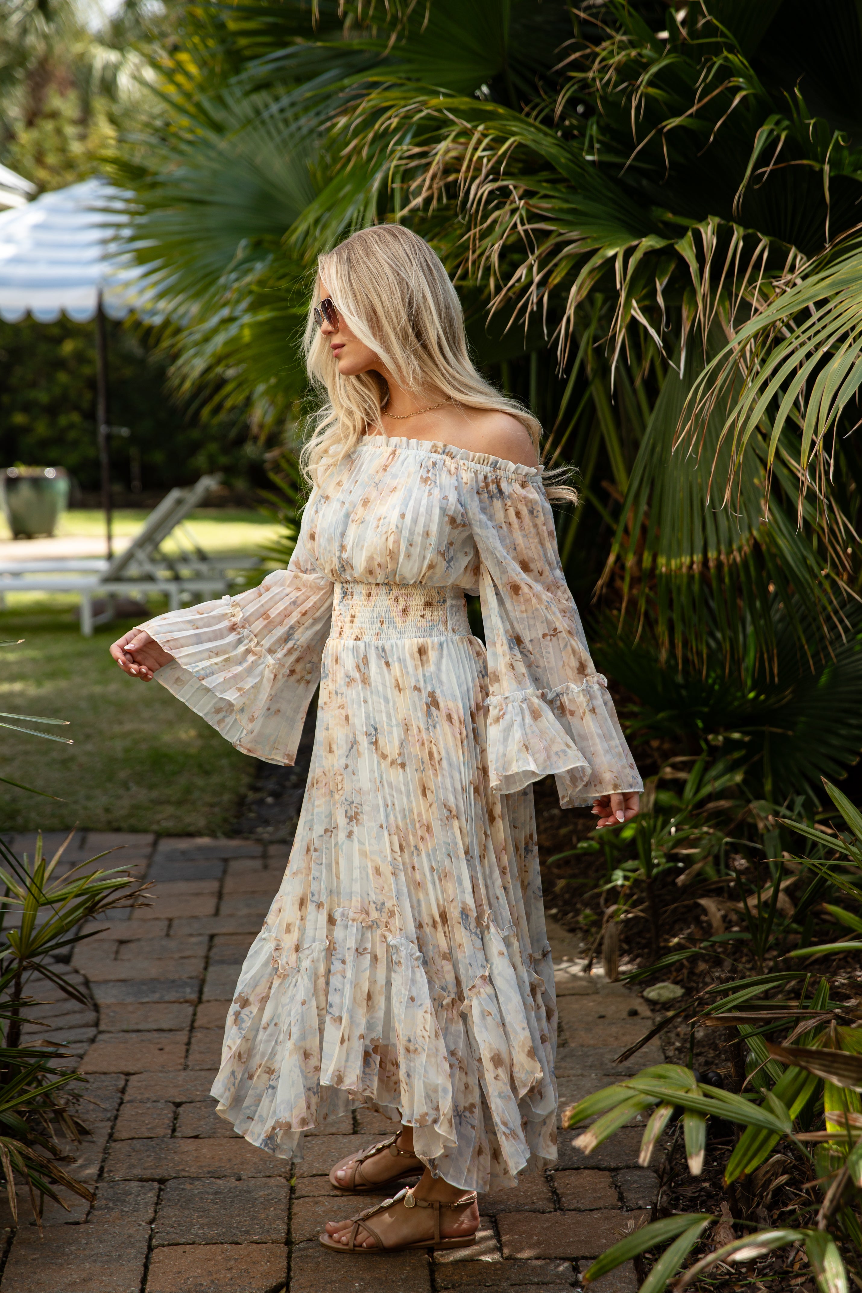 Woman in a floral off-shoulder dress standing outdoors with greenery around