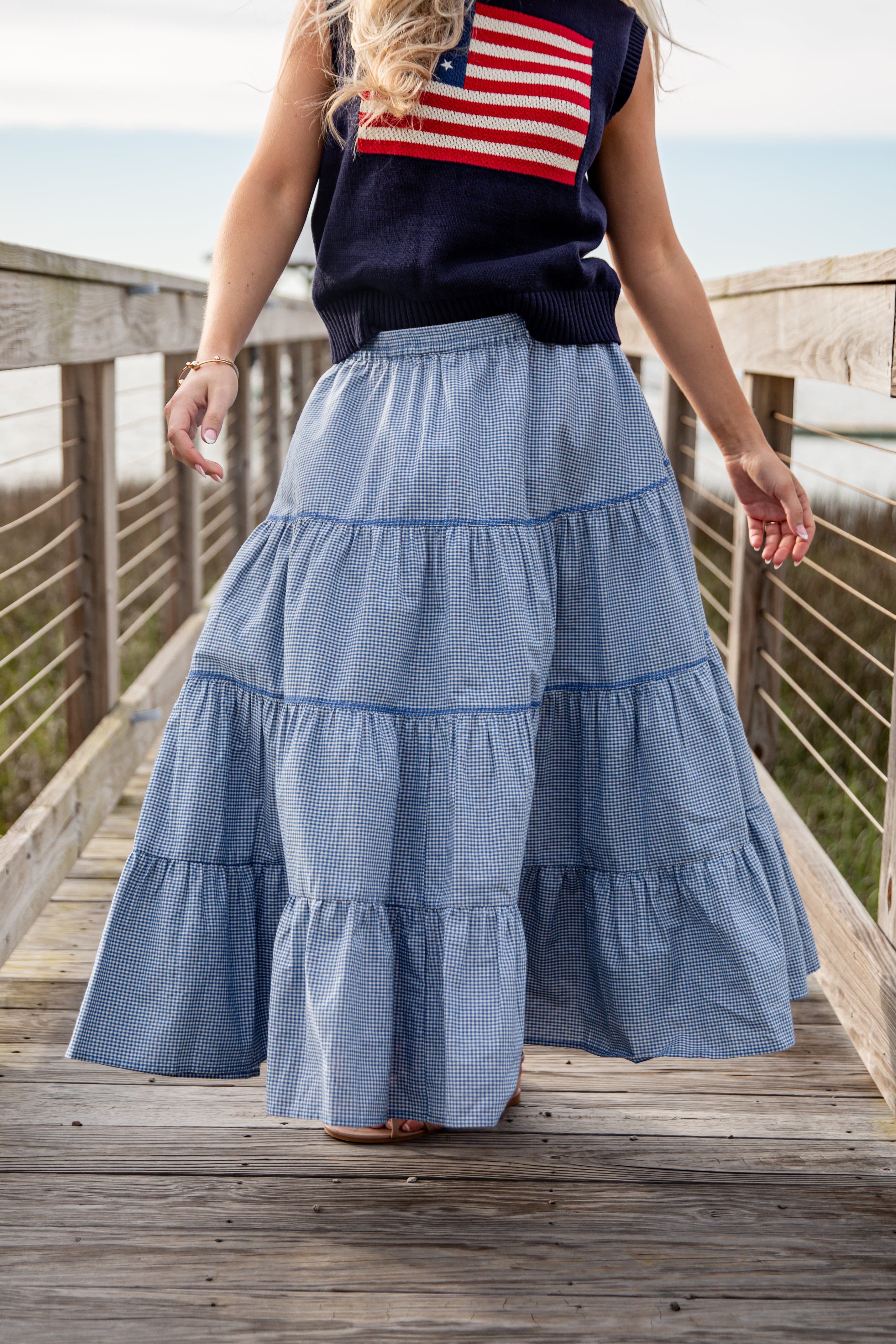 Person wearing a blue tiered skirt and American flag top on a wooden deck.