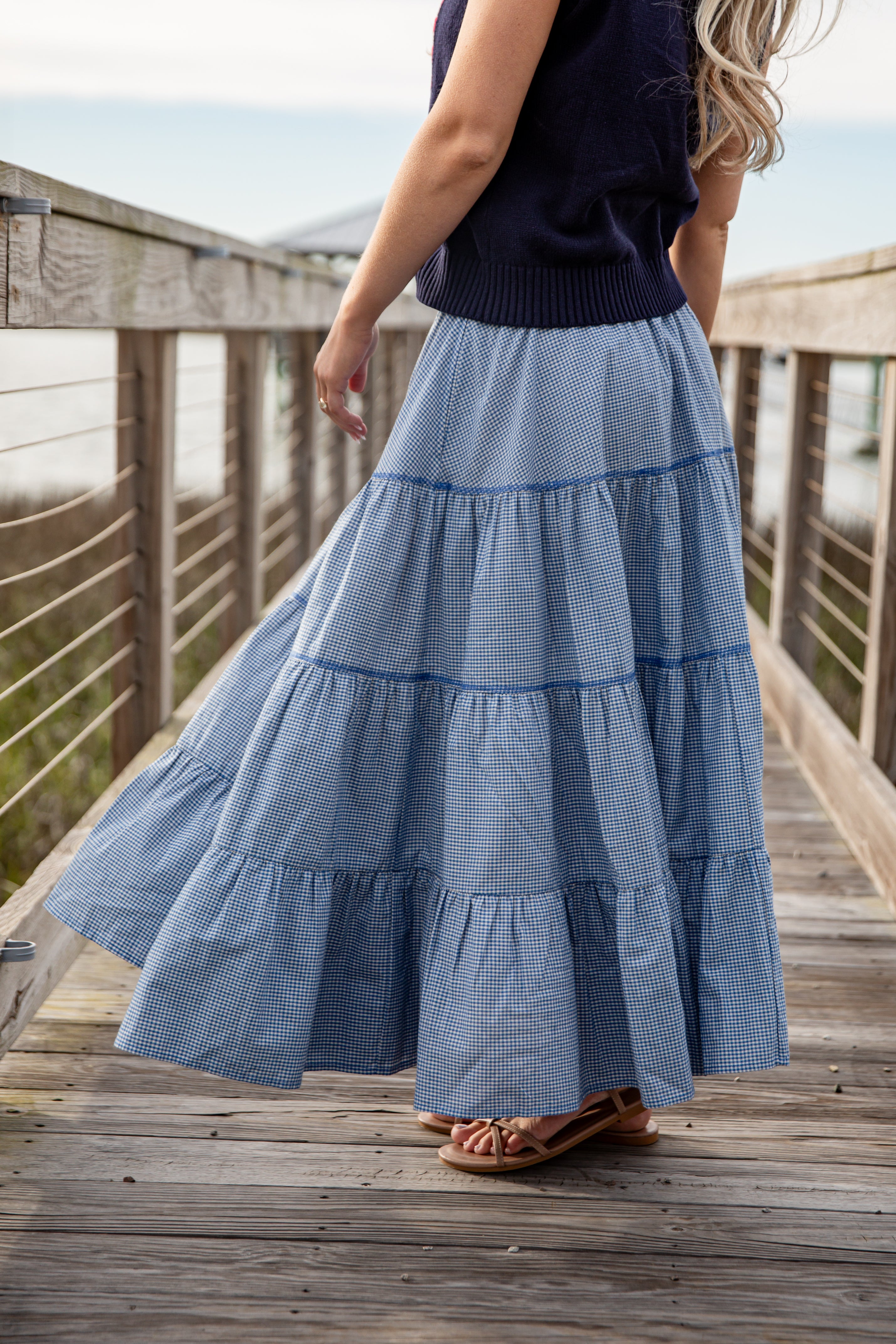 Person wearing a long blue tiered skirt on a wooden deck.