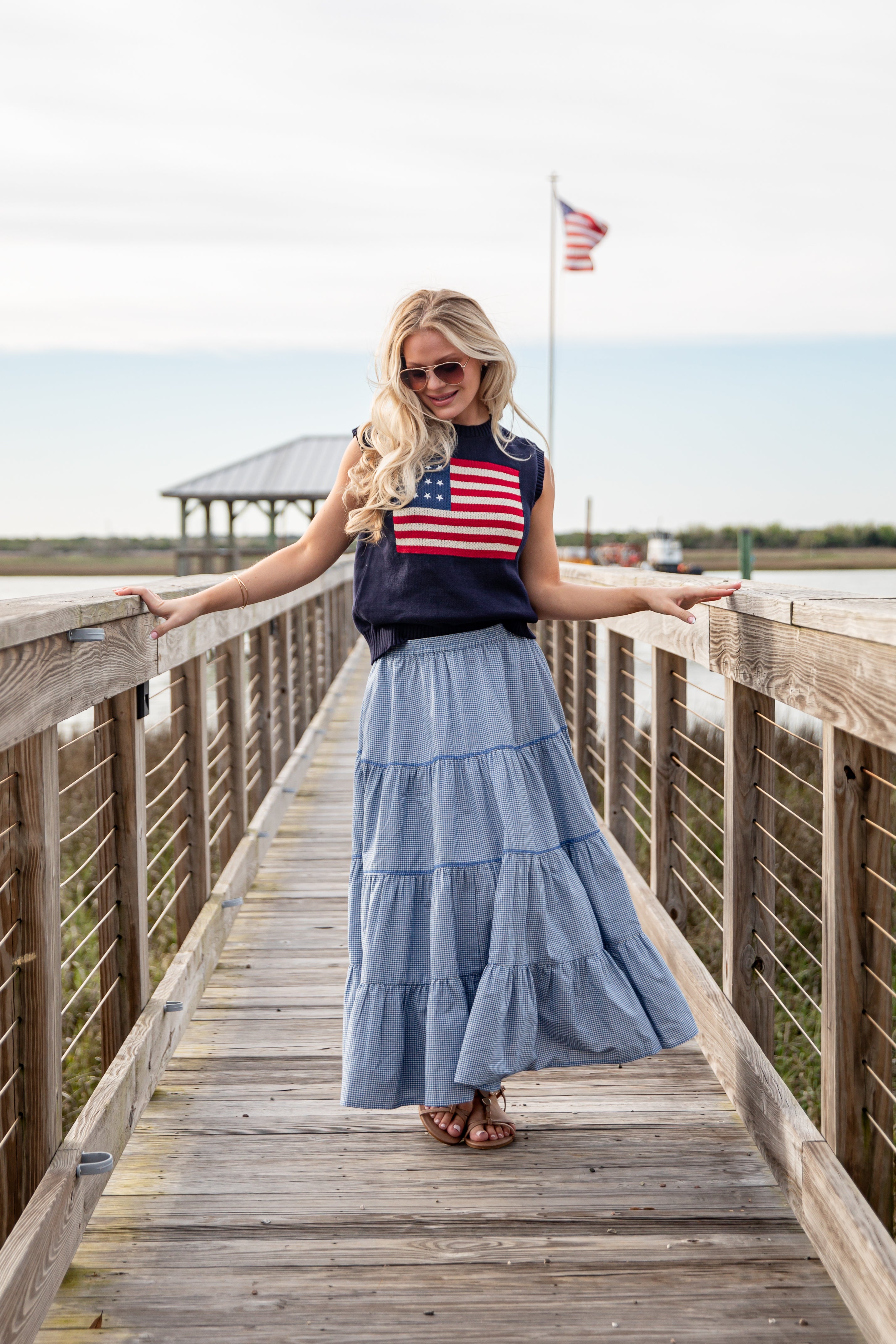 Woman standing on a wooden boardwalk wearing an American flag top and blue skirt.