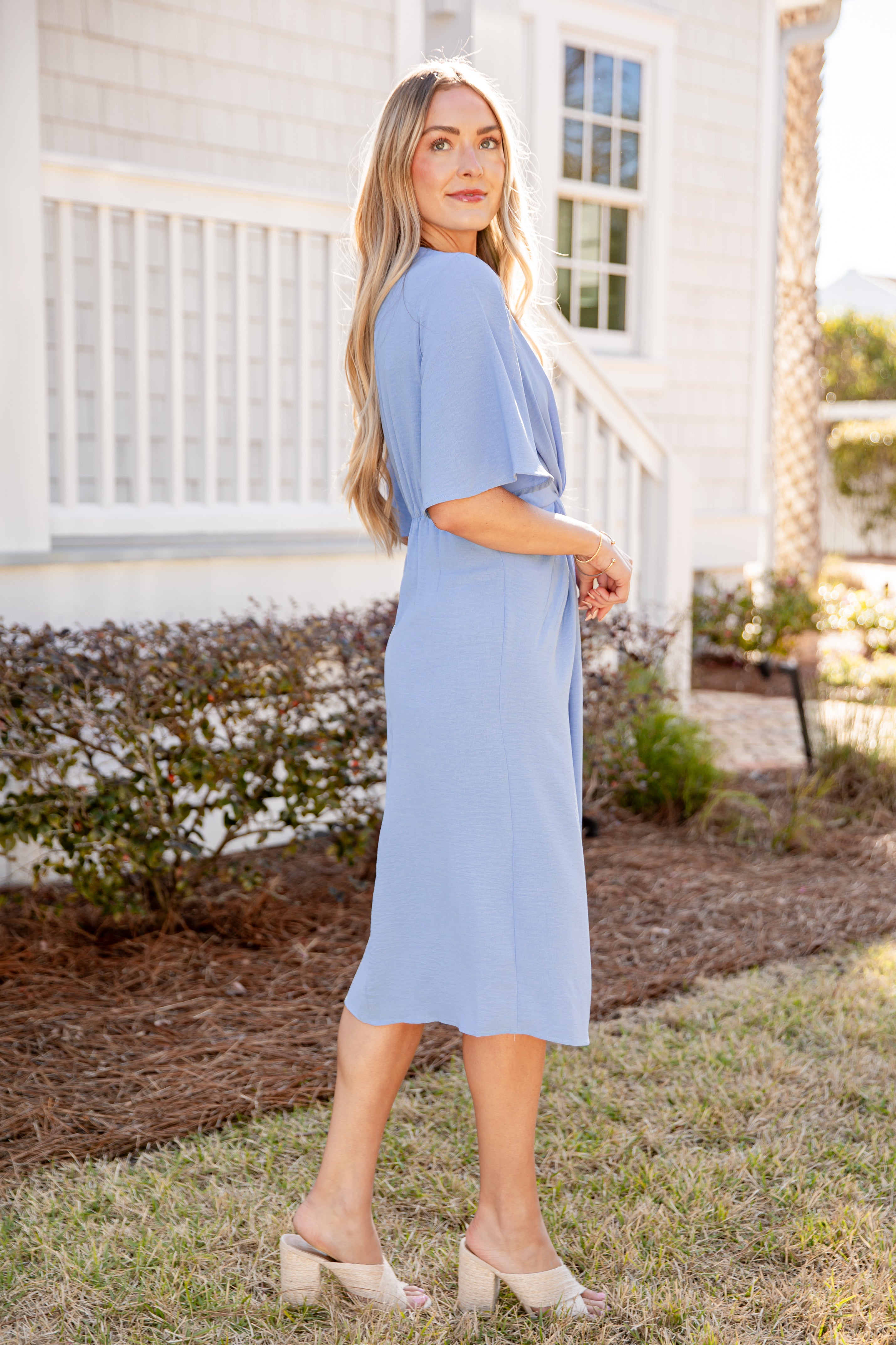 Woman in a light blue dress standing outdoors near a white house.