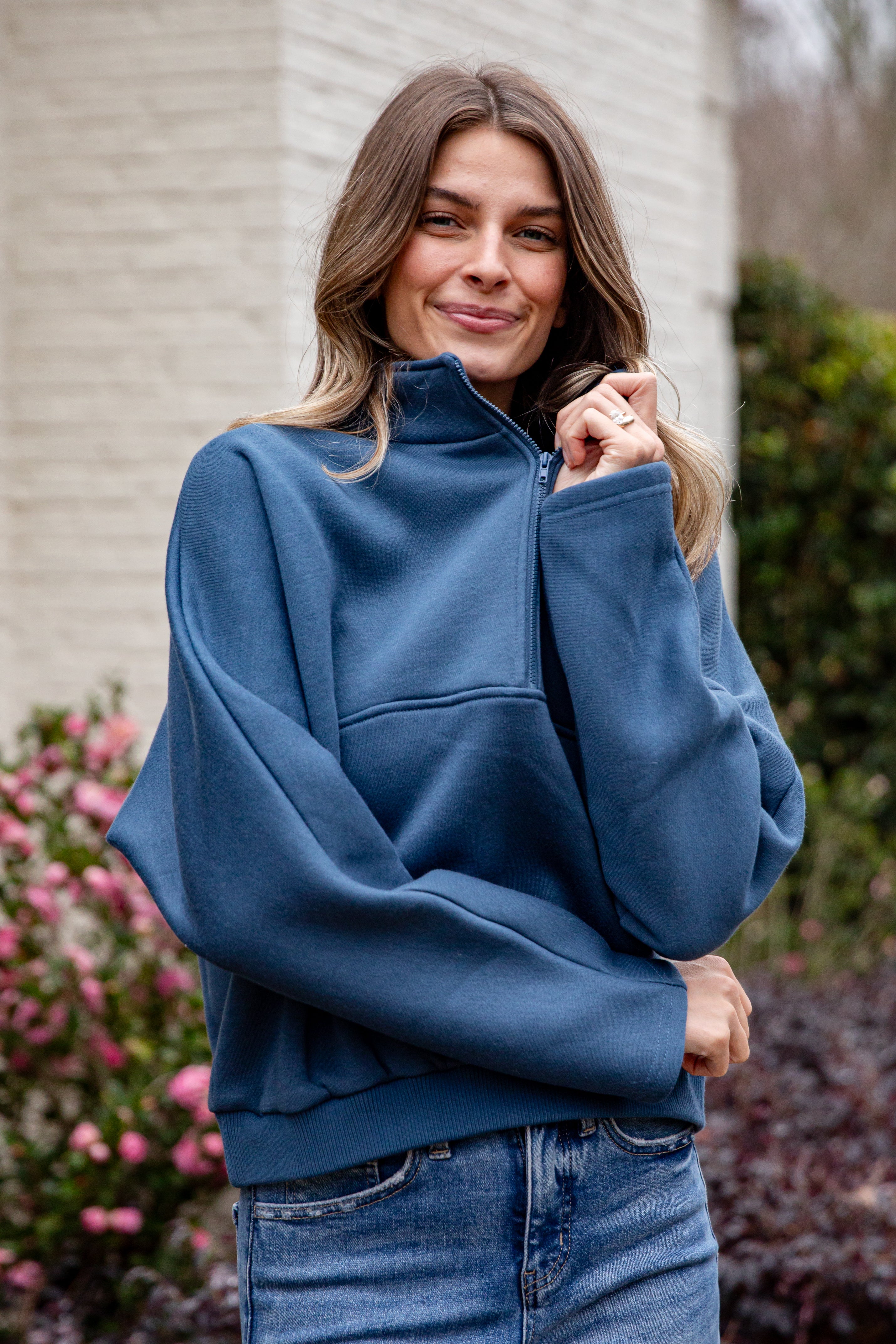 Woman wearing a blue pullover with a zipper, standing outdoors.