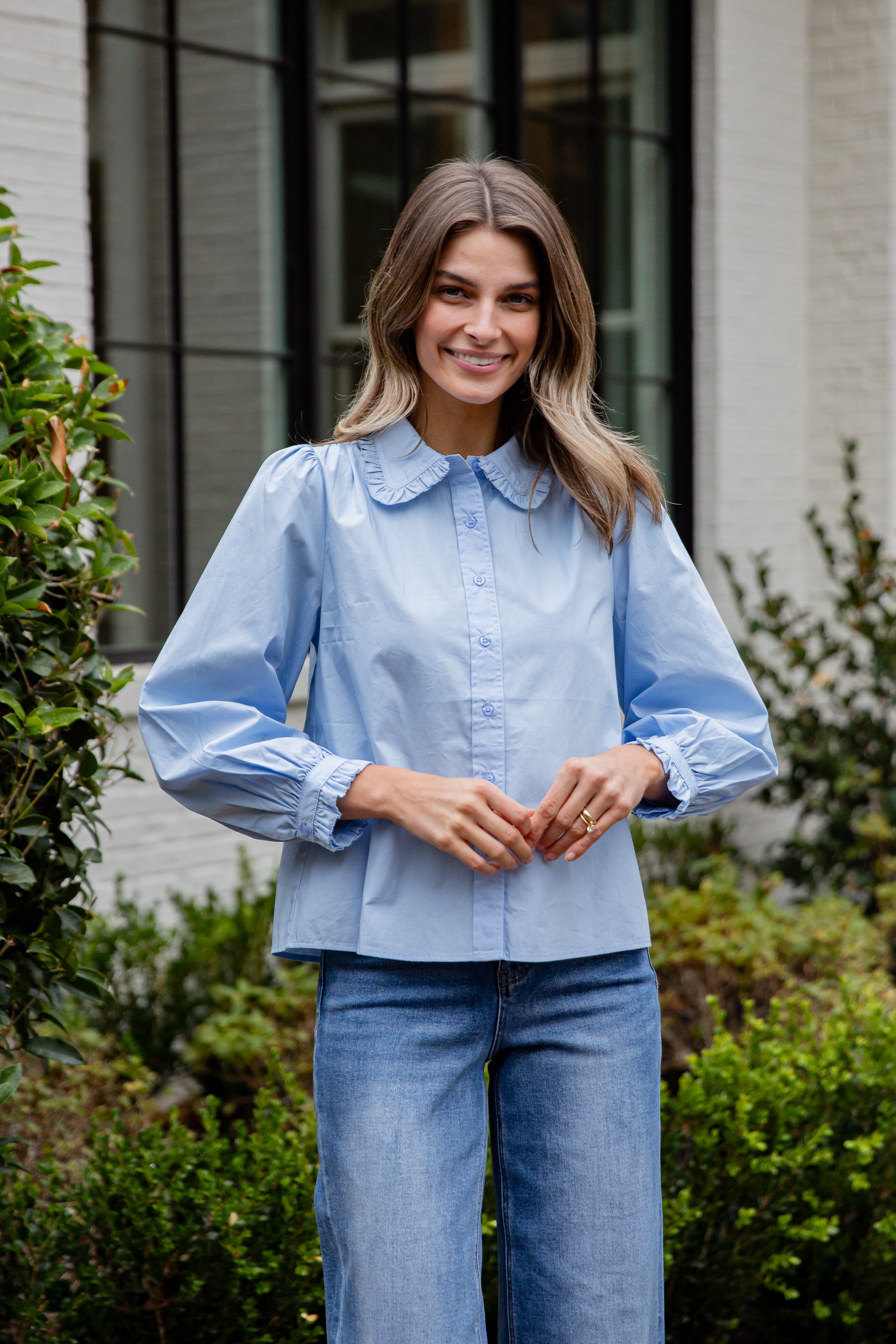 Woman wearing a light blue shirt and jeans standing outdoors.