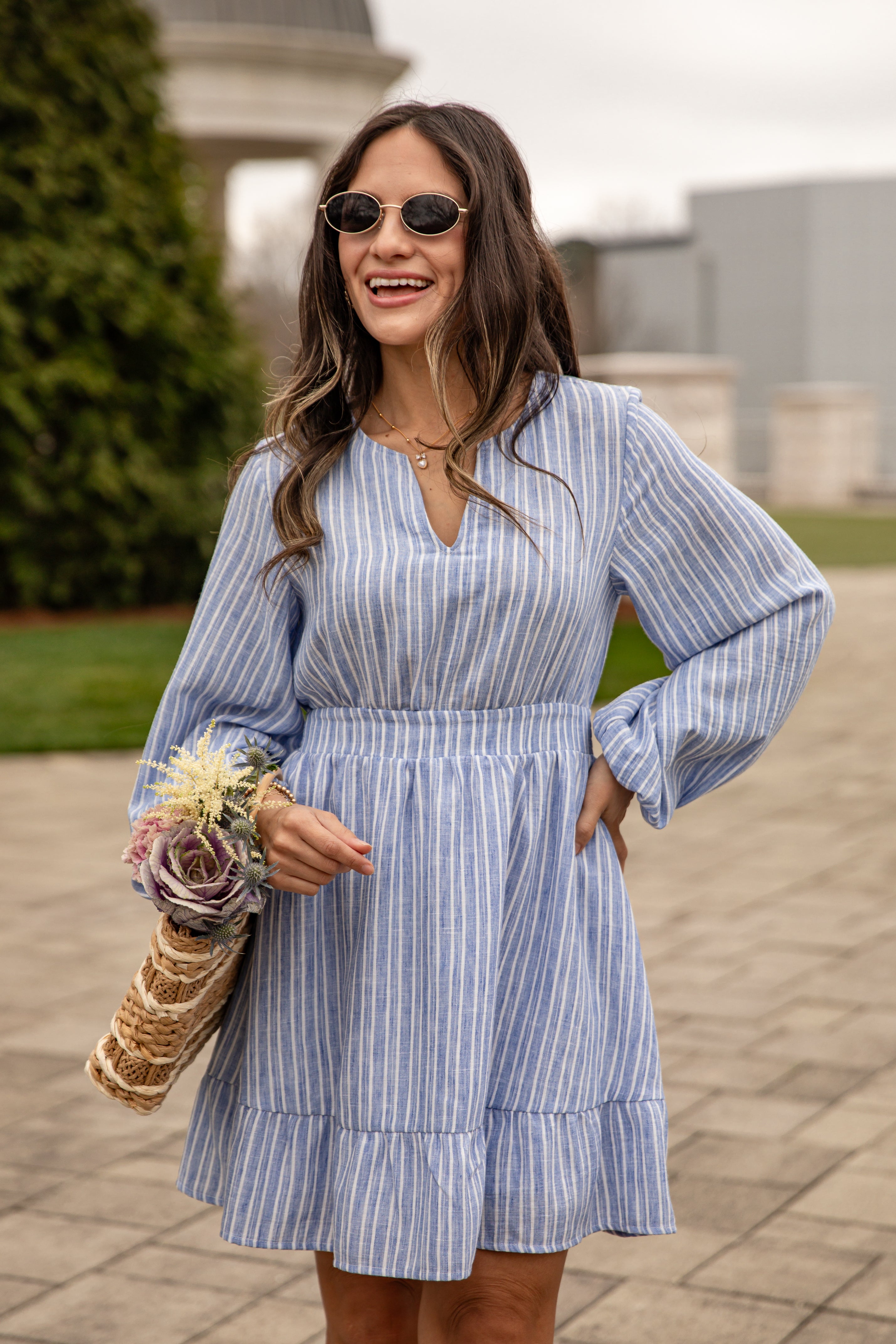 Woman wearing a blue striped dress holding flowers outdoors.