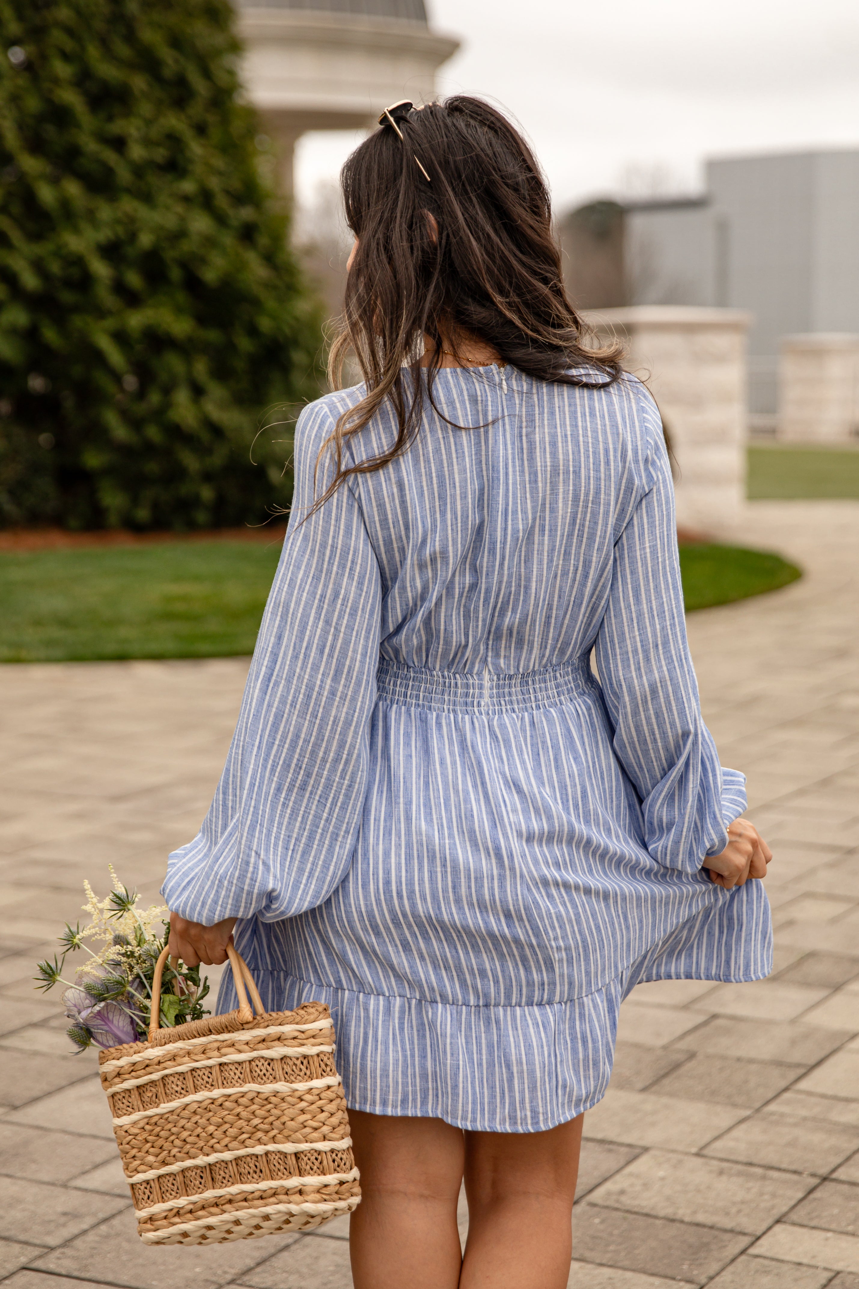 Woman in a blue striped dress holding a woven bag outdoors.