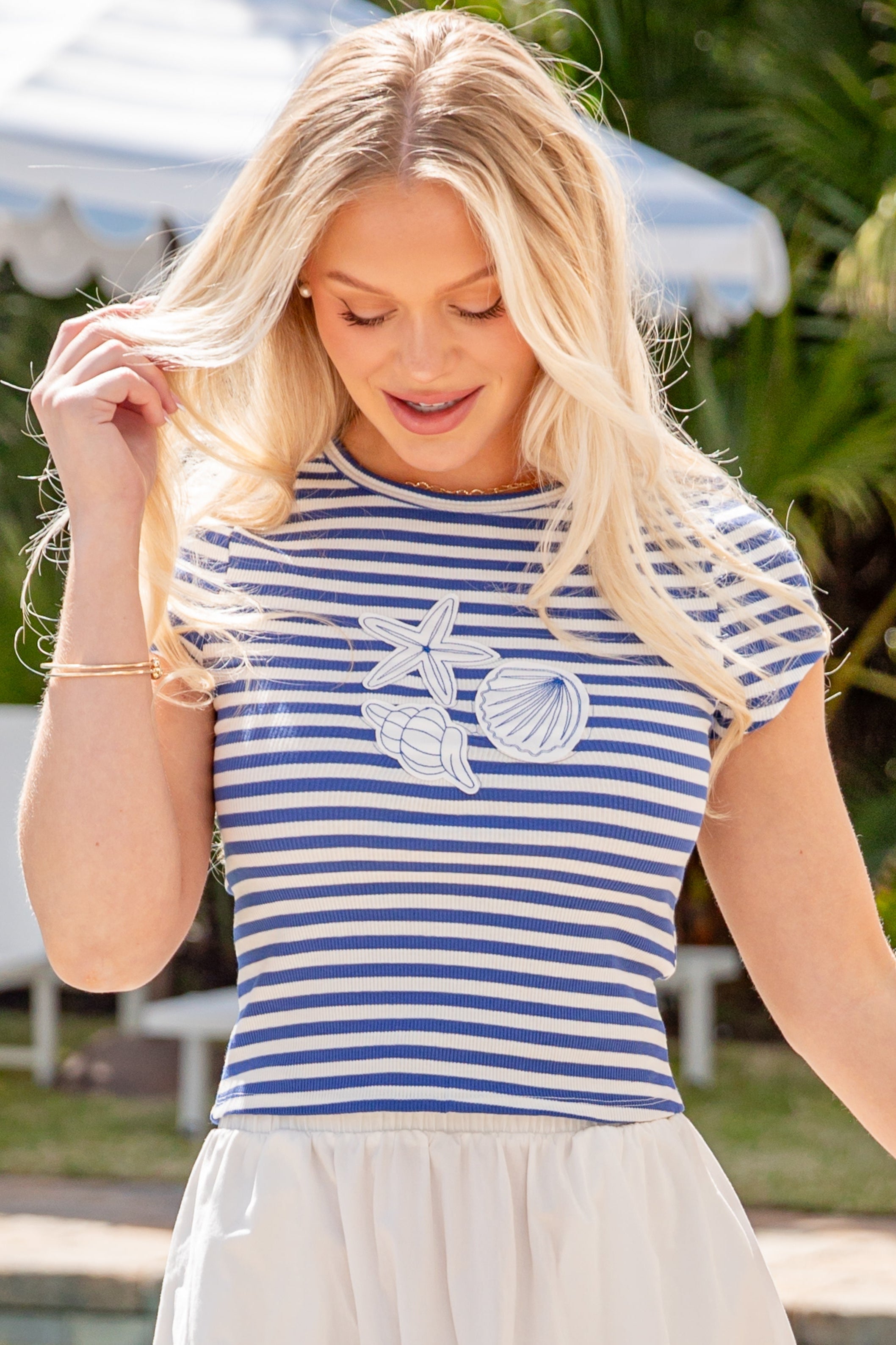 Woman wearing a blue and white striped shirt with a graphic design, standing outdoors near a pool.