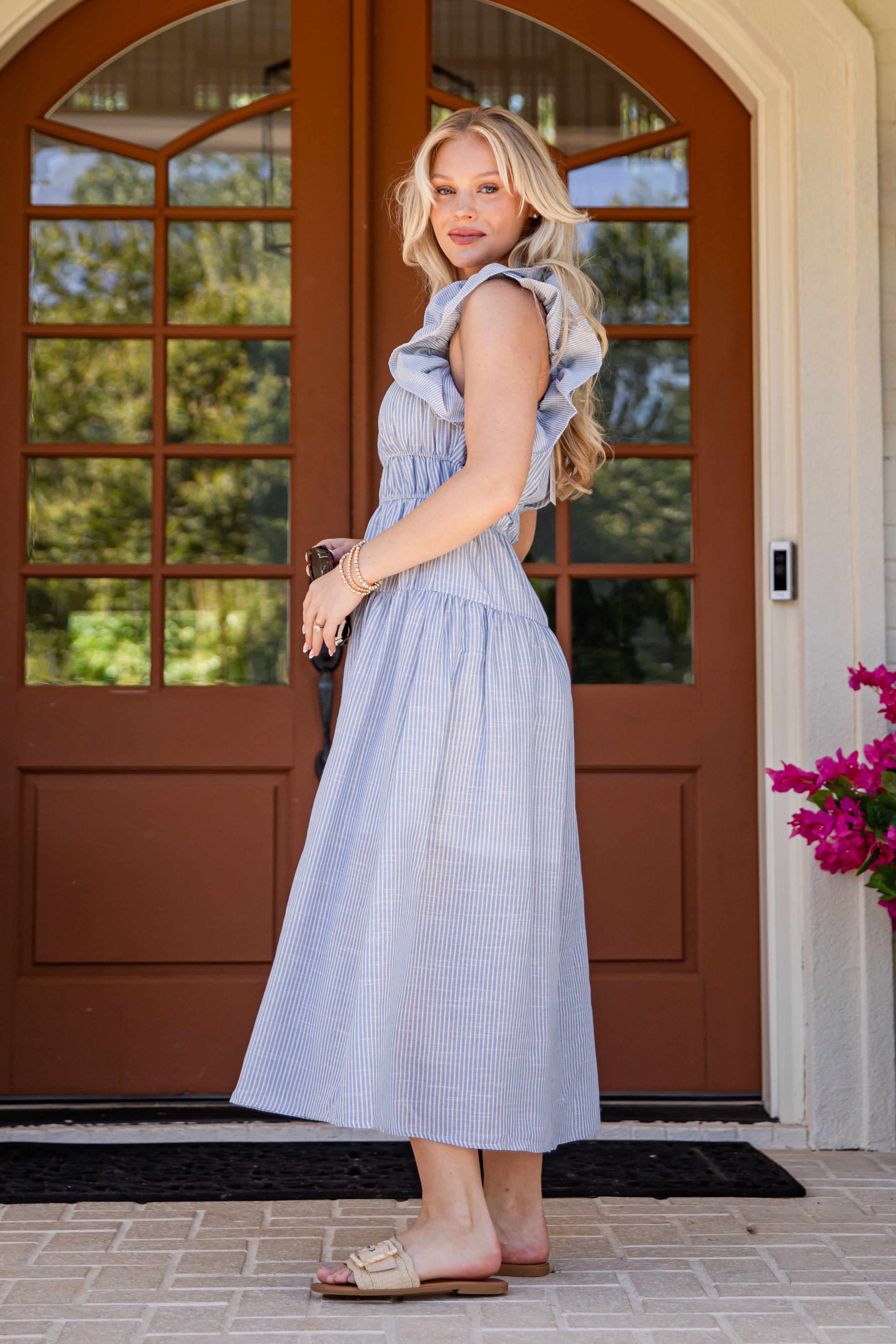 Woman in a light blue dress standing in front of a brown door with glass panels.