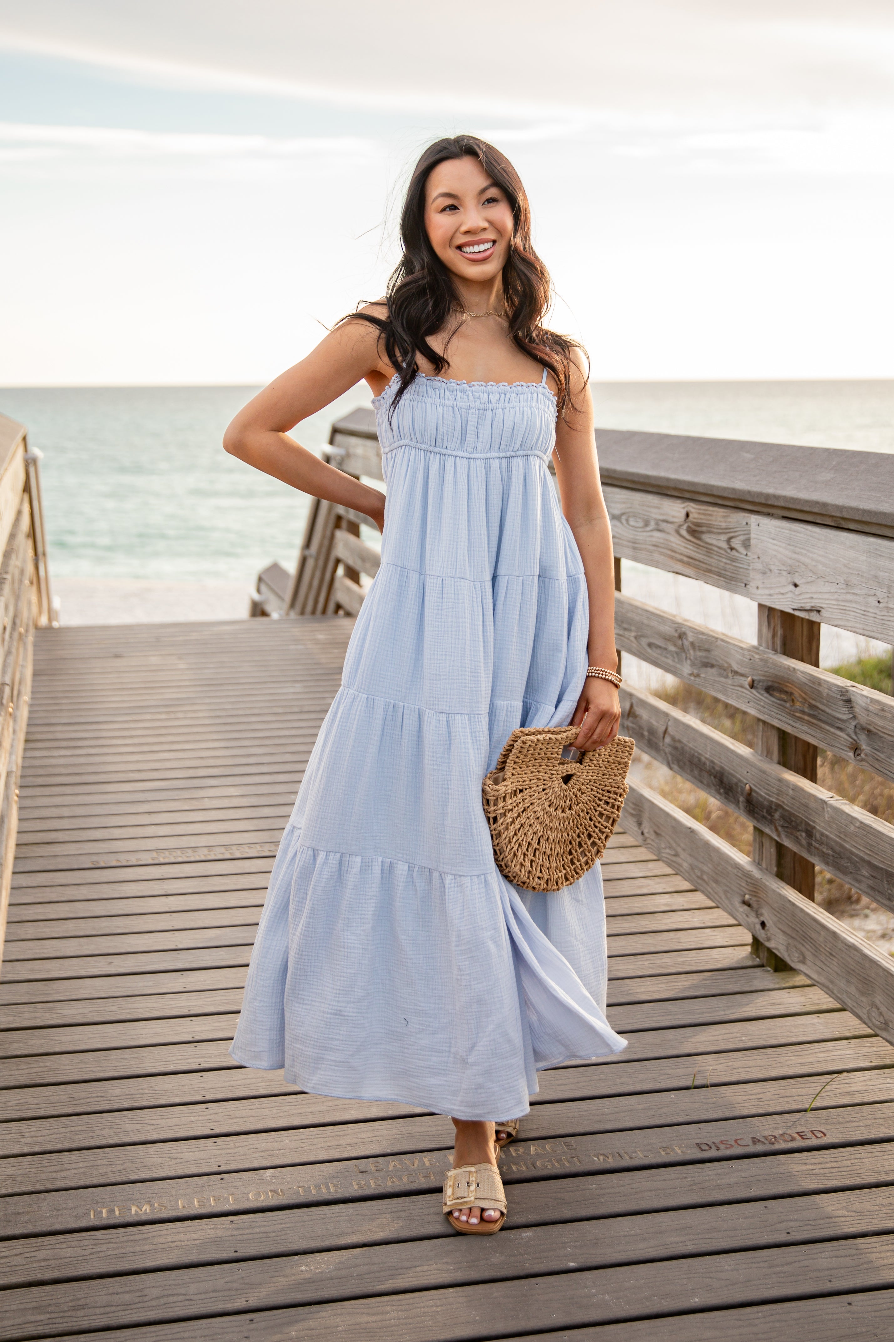 Woman in a light blue dress standing on a wooden boardwalk by the beach
