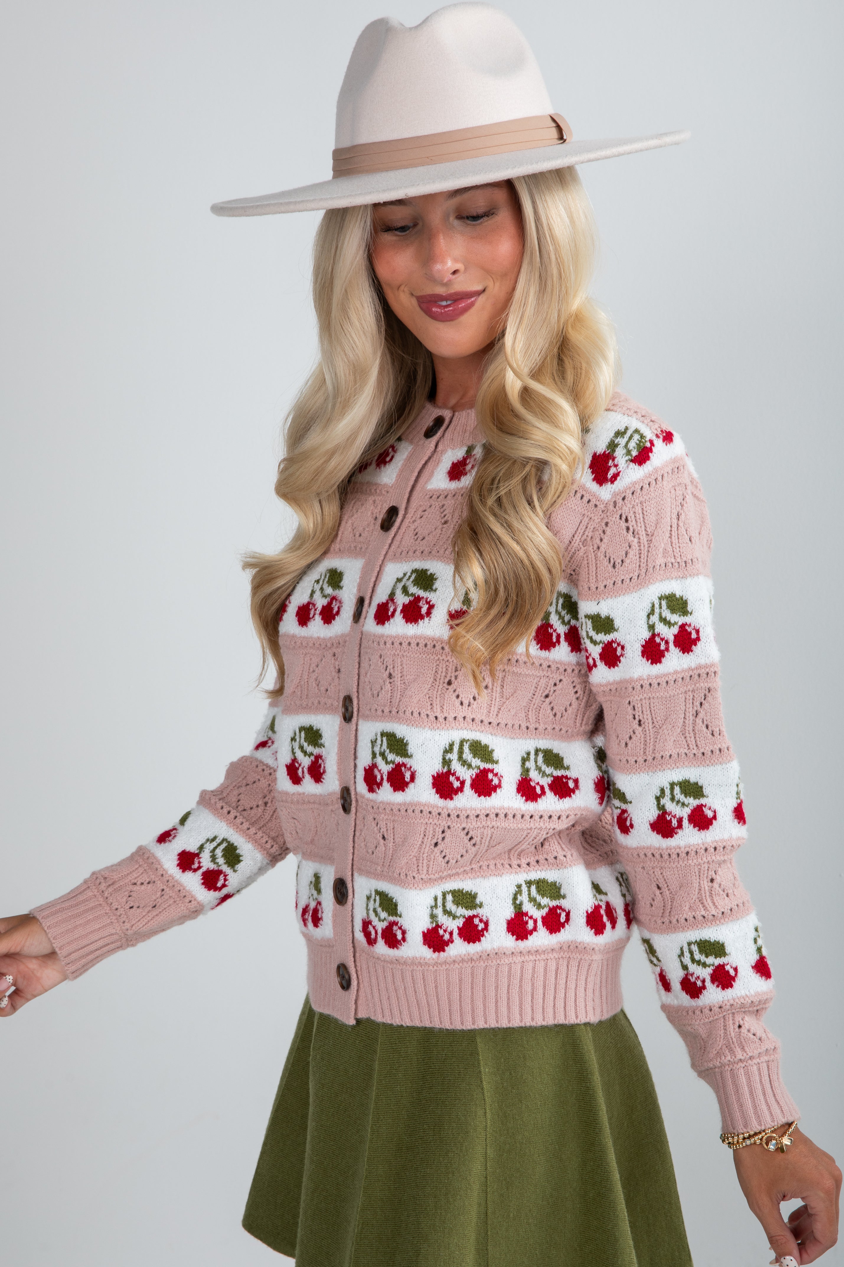 Woman wearing a pink sweater with cherry pattern and a white hat on a light gray background